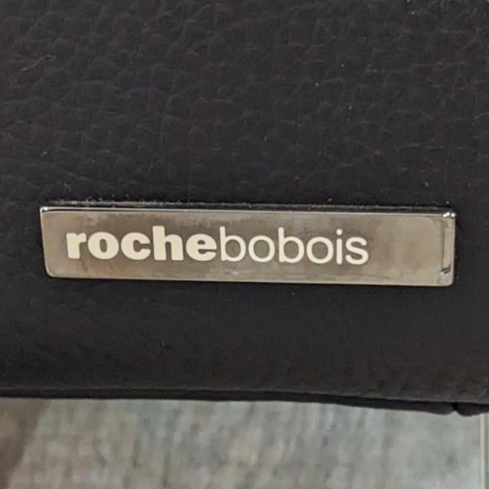 Close-up of Roche Bobois logo on black leather loveseat showcasing brand identity.