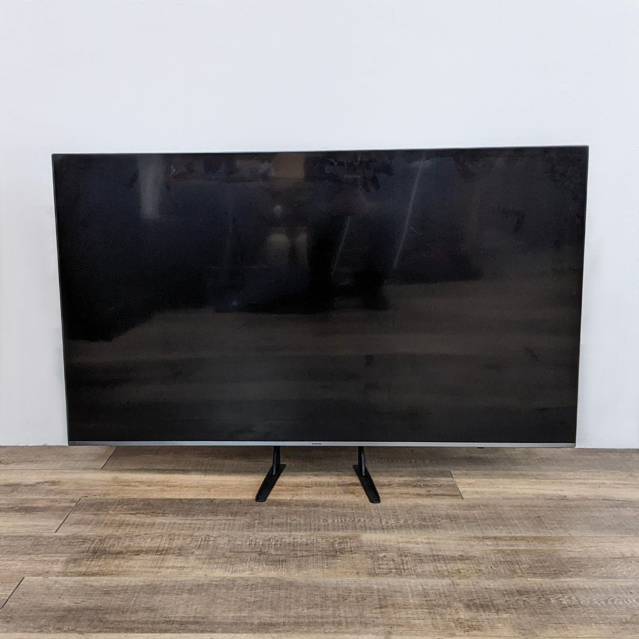 1. Samsung TV displayed on a wooden floor with a black screen reflecting the surrounding room.