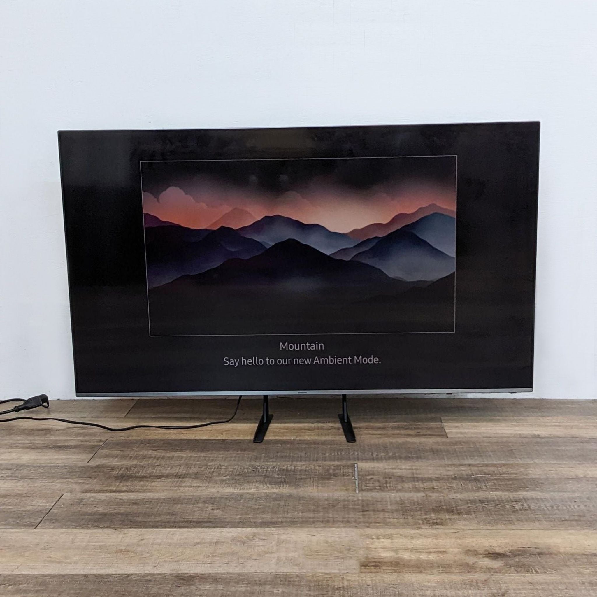 2. Samsung television showcasing Ambient Mode with a mountain scene on the screen, placed on a wooden floor.