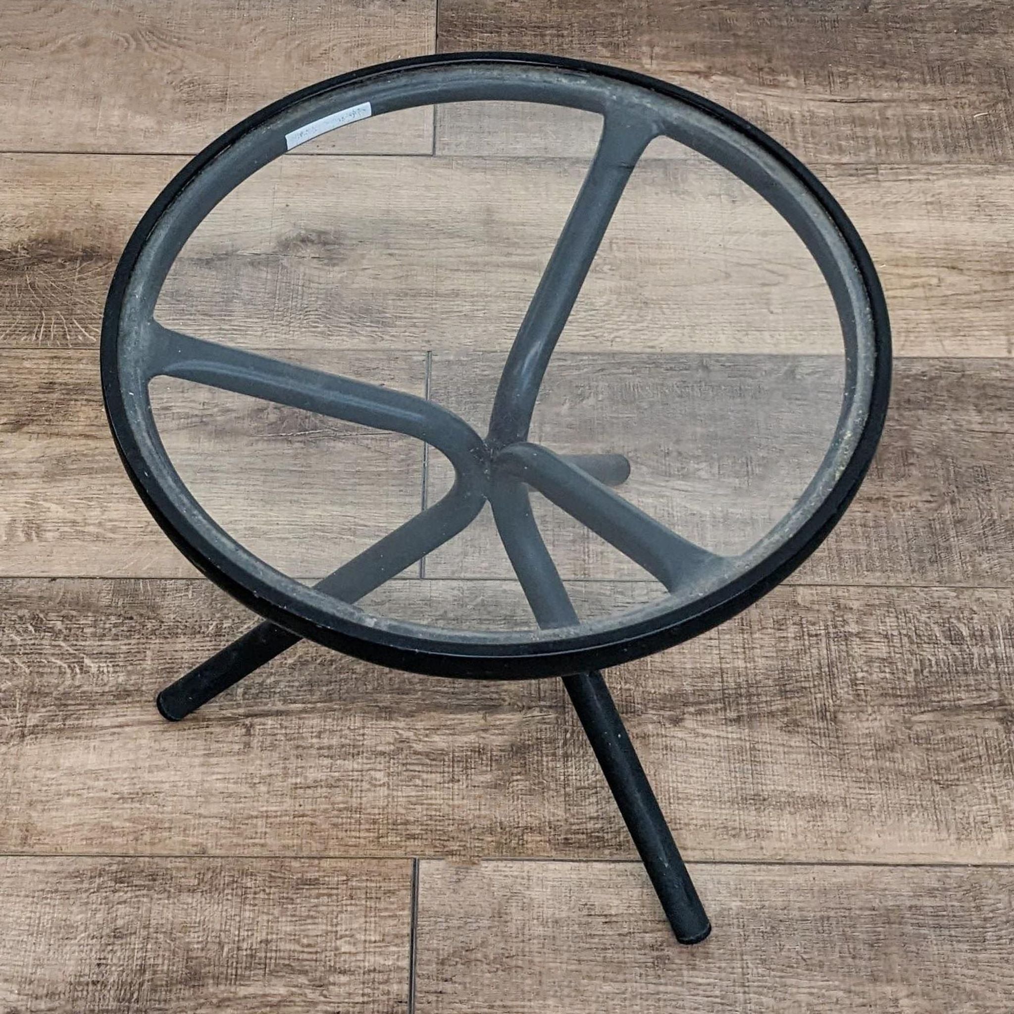 Brown Jordan 18" round aluminum accent table with glass top, featuring a three-legged base, viewed from the top on a wooden floor.