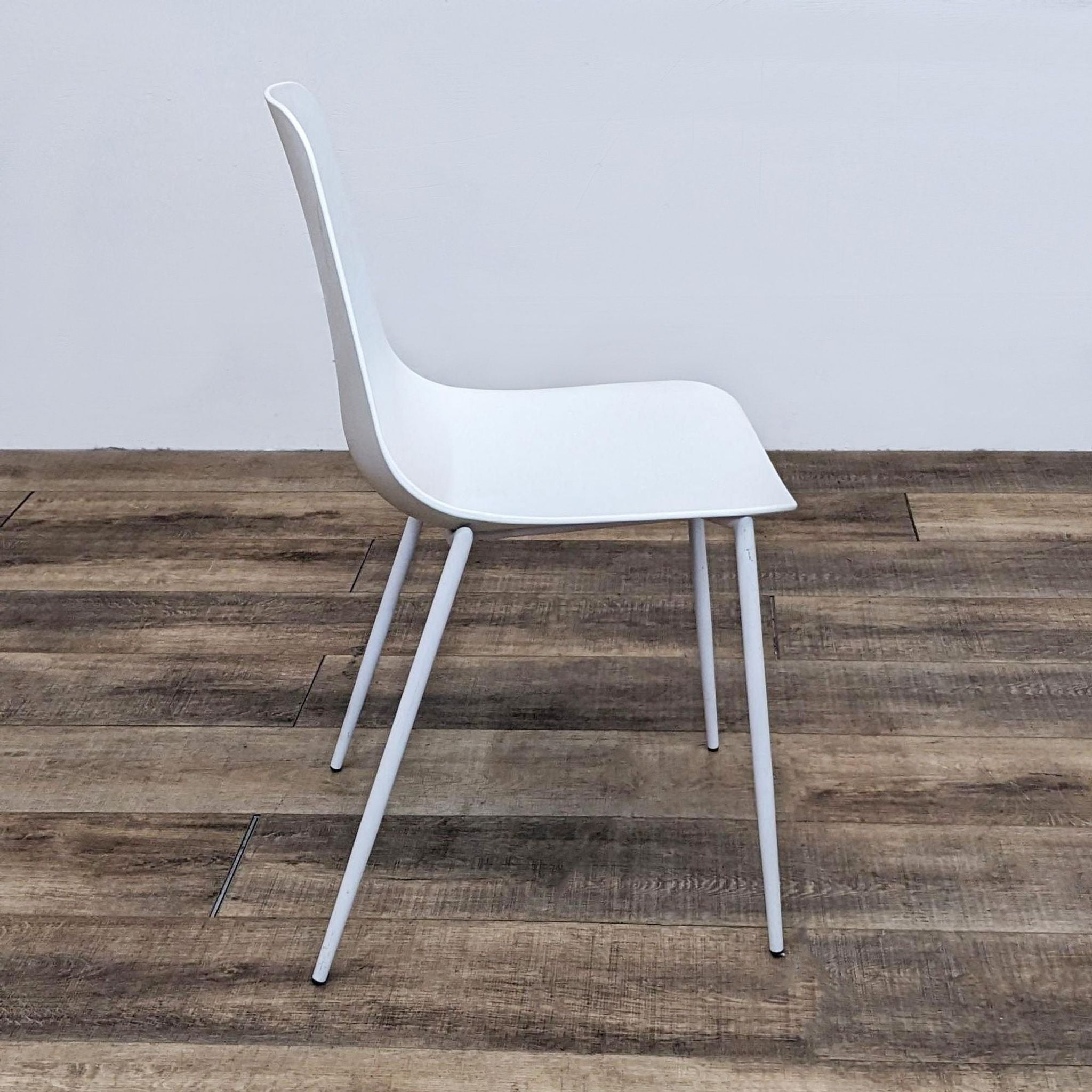 Angled view of white Reperch polypropylene side chair with slender legs, wooden floor backdrop.