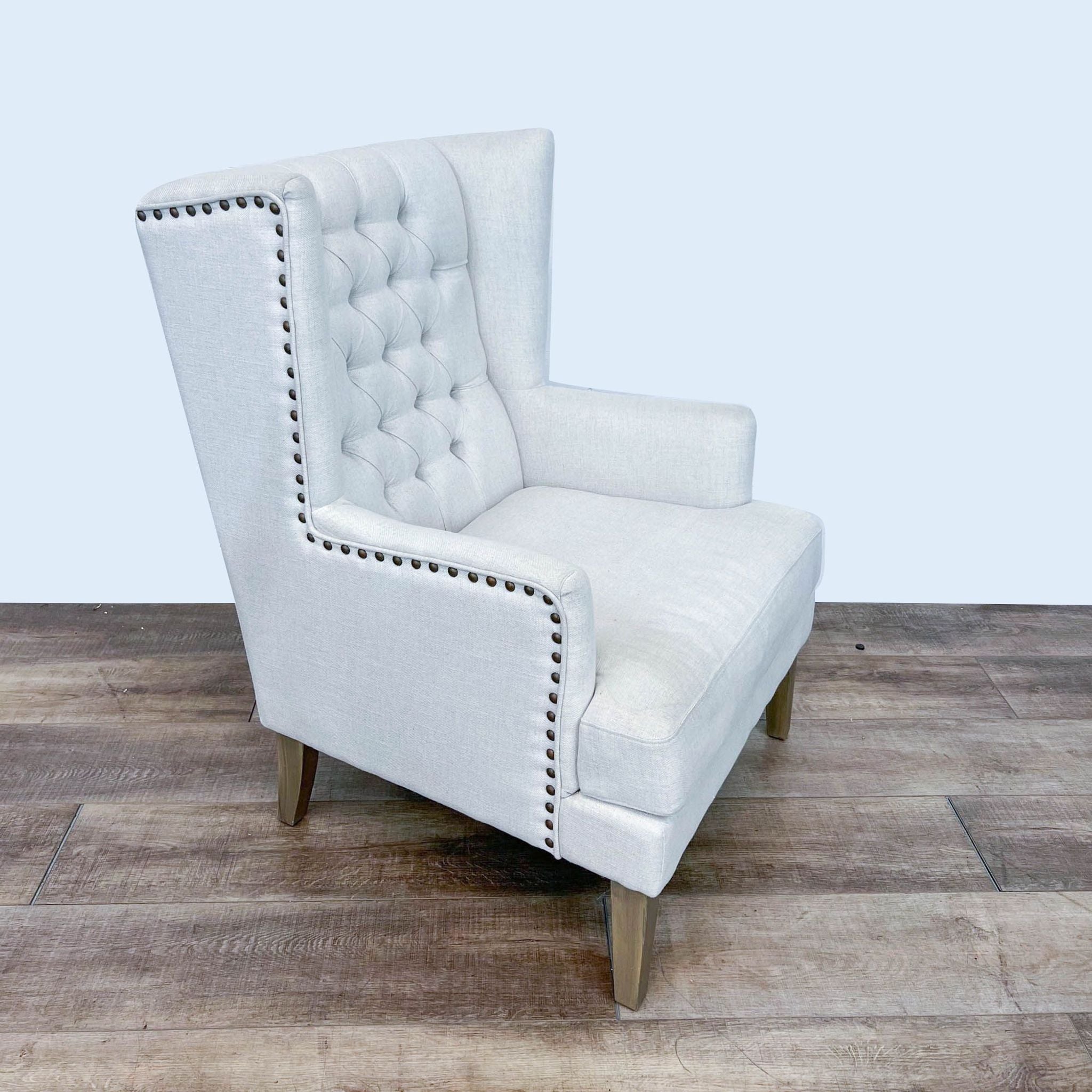 Arhaus contemporary style wingback chair with textured fabric, button tufting, nailhead trim, and tapered wood legs.