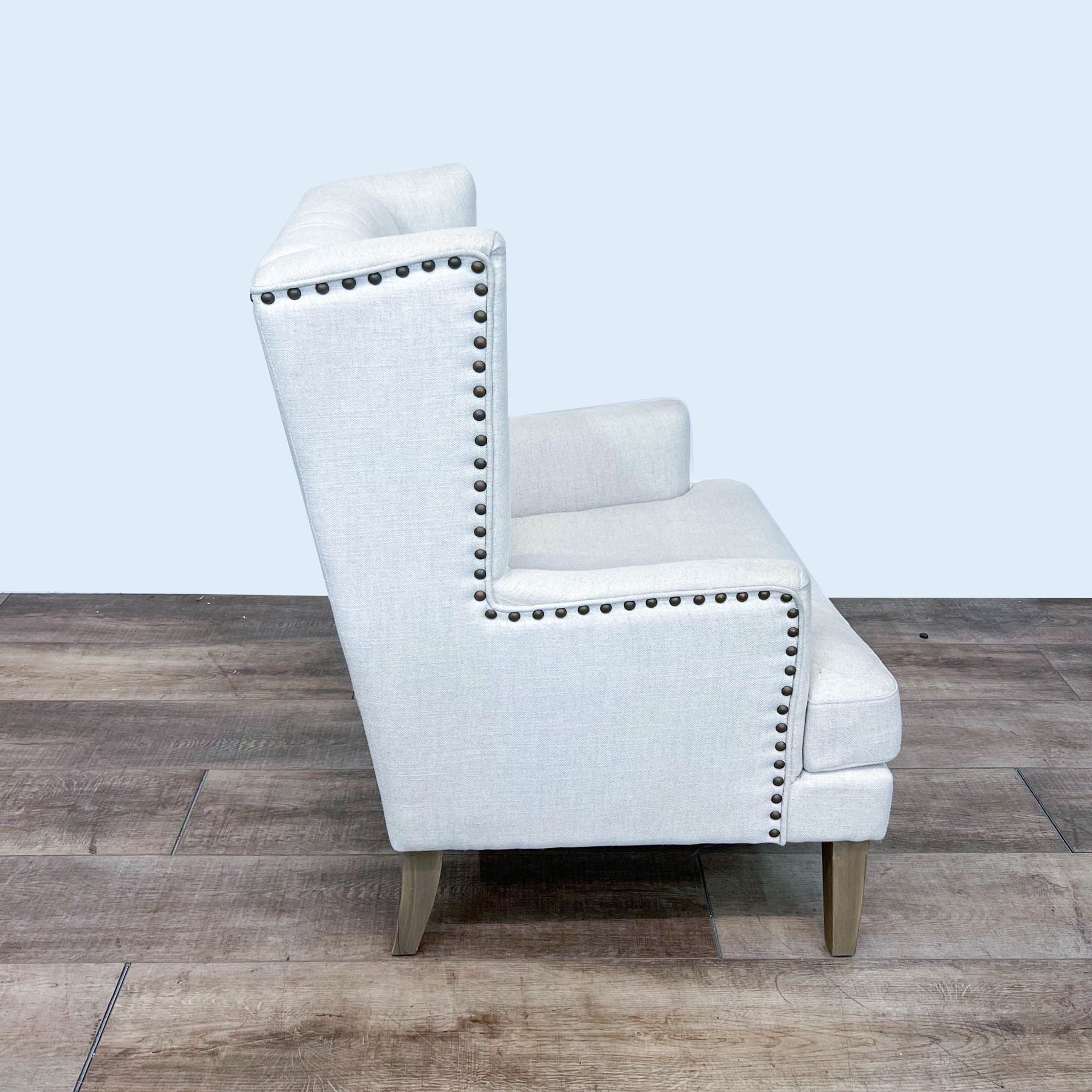 Textured fabric upholstered Arhaus lounge chair with tufted backrest and nailhead trim, showcasing tapered wood legs.