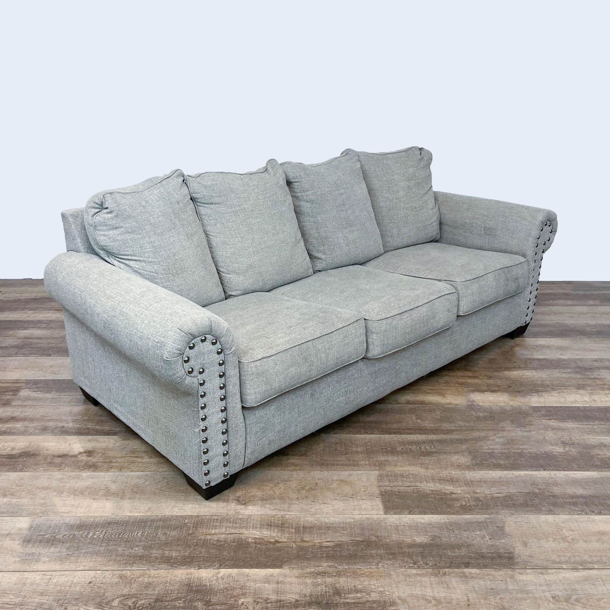 Ashley Furniture gray roll arm sleeper sofa with queen mattress and nailhead details on a wooden floor.