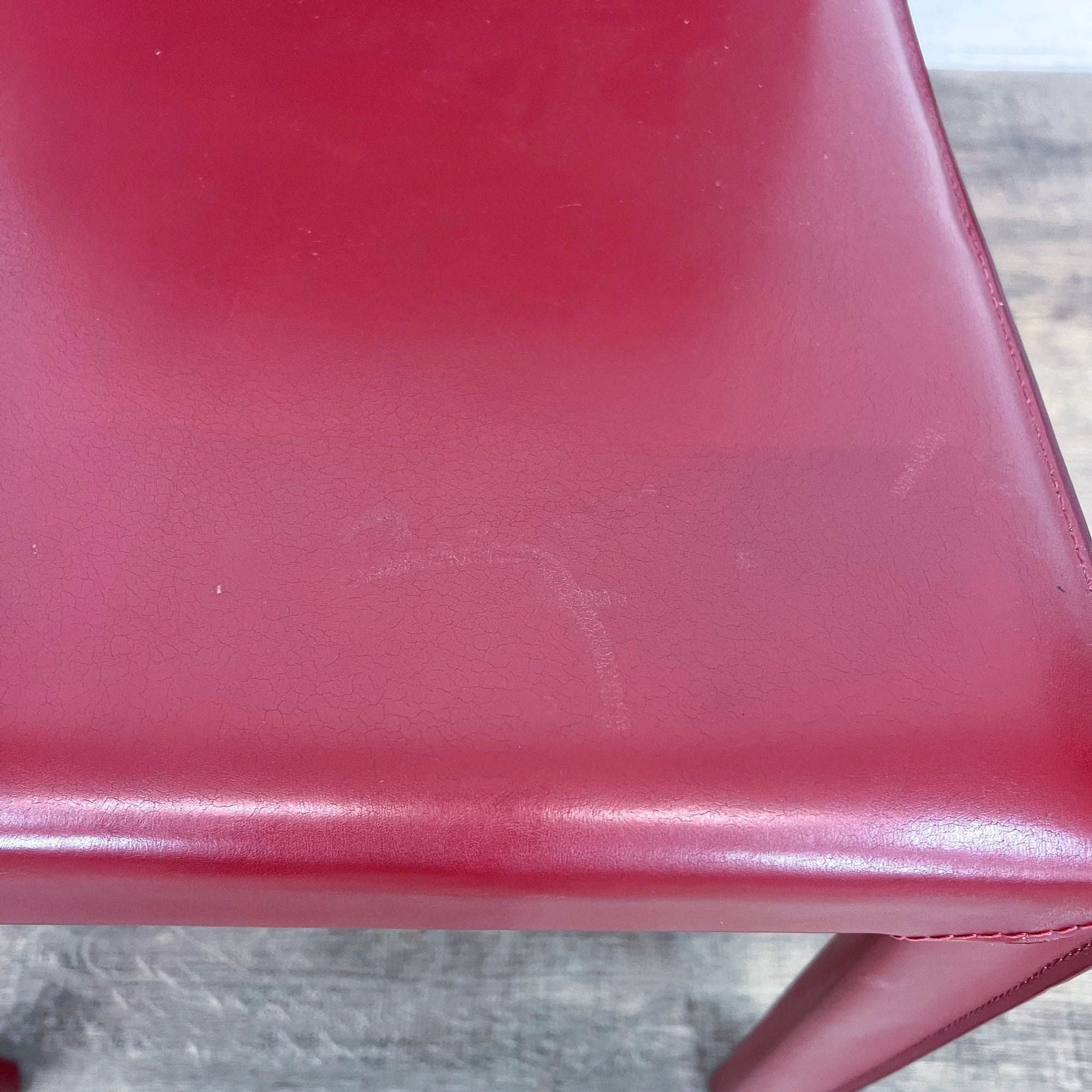 Close-up of a red bonded leather upholstered Maria Yee modern dining chair with curved back detail.
