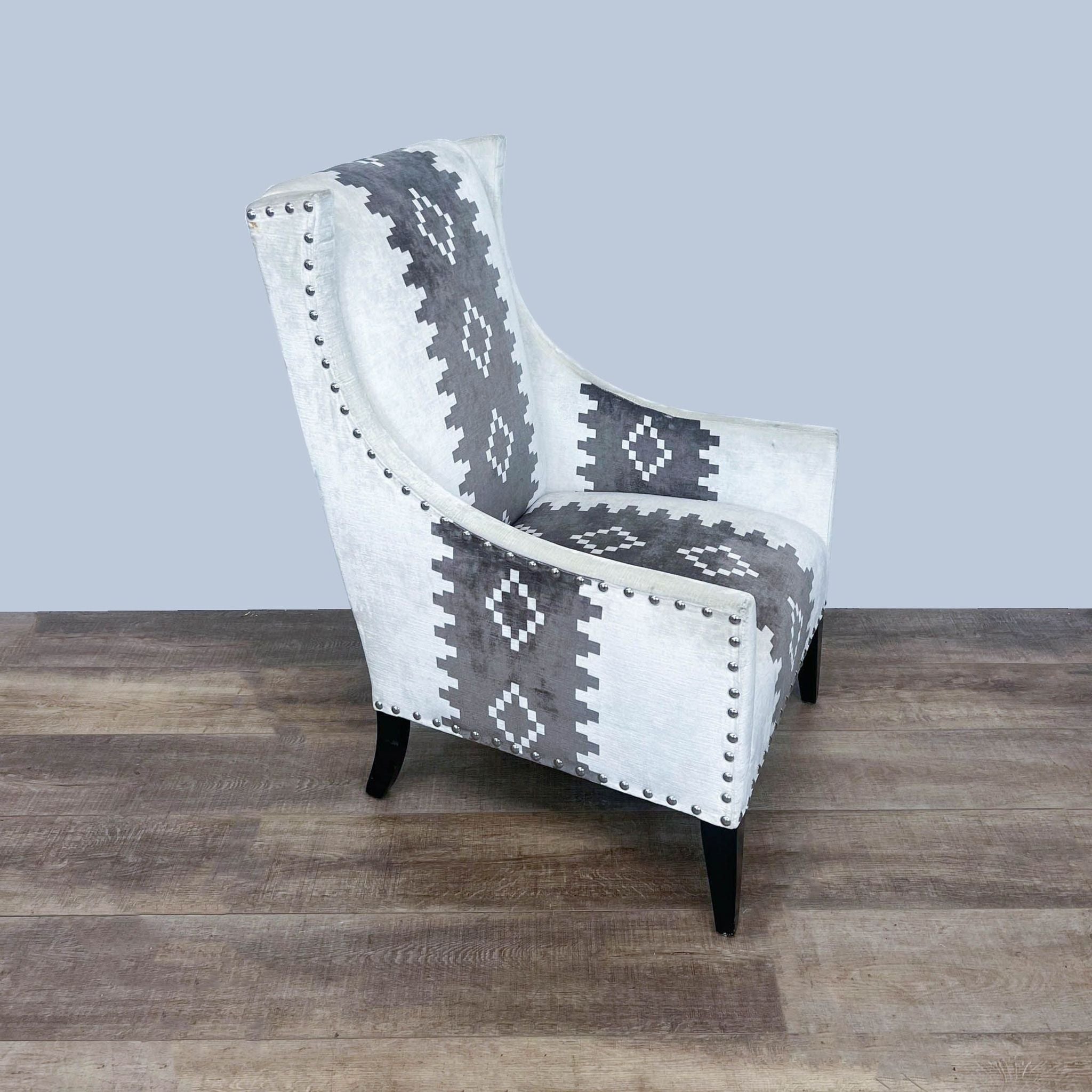 Western print upholstered Pluto chair by Andrew Martin with padded seat and nailhead trim, angled view on wooden flooring.