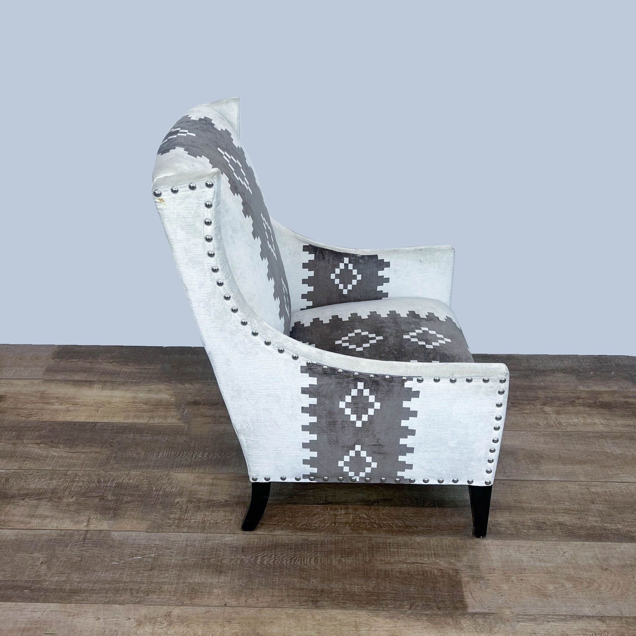 High-backed Andrew Martin Pluto chair with western print fabric and nailhead trim on a wooden floor.