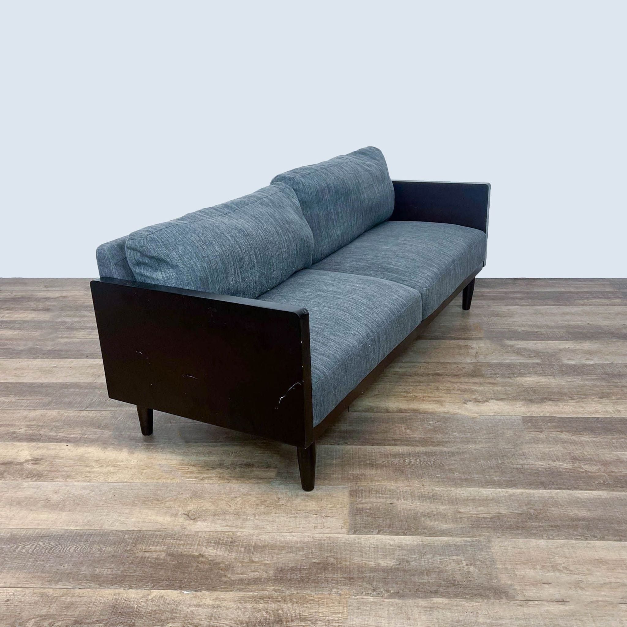 Angle view of a Noble Home loveseat in gray fabric with dark wood details, showcasing side and wooden legs.