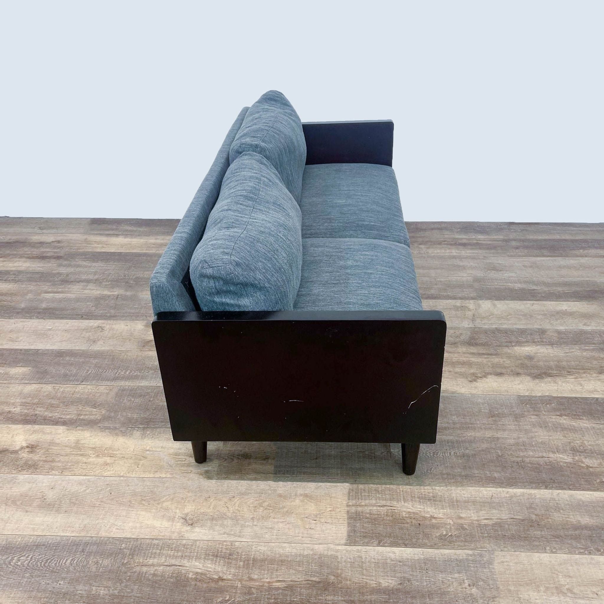 Gray Noble Home loveseat with dark wood arms and feet on a wooden floor.