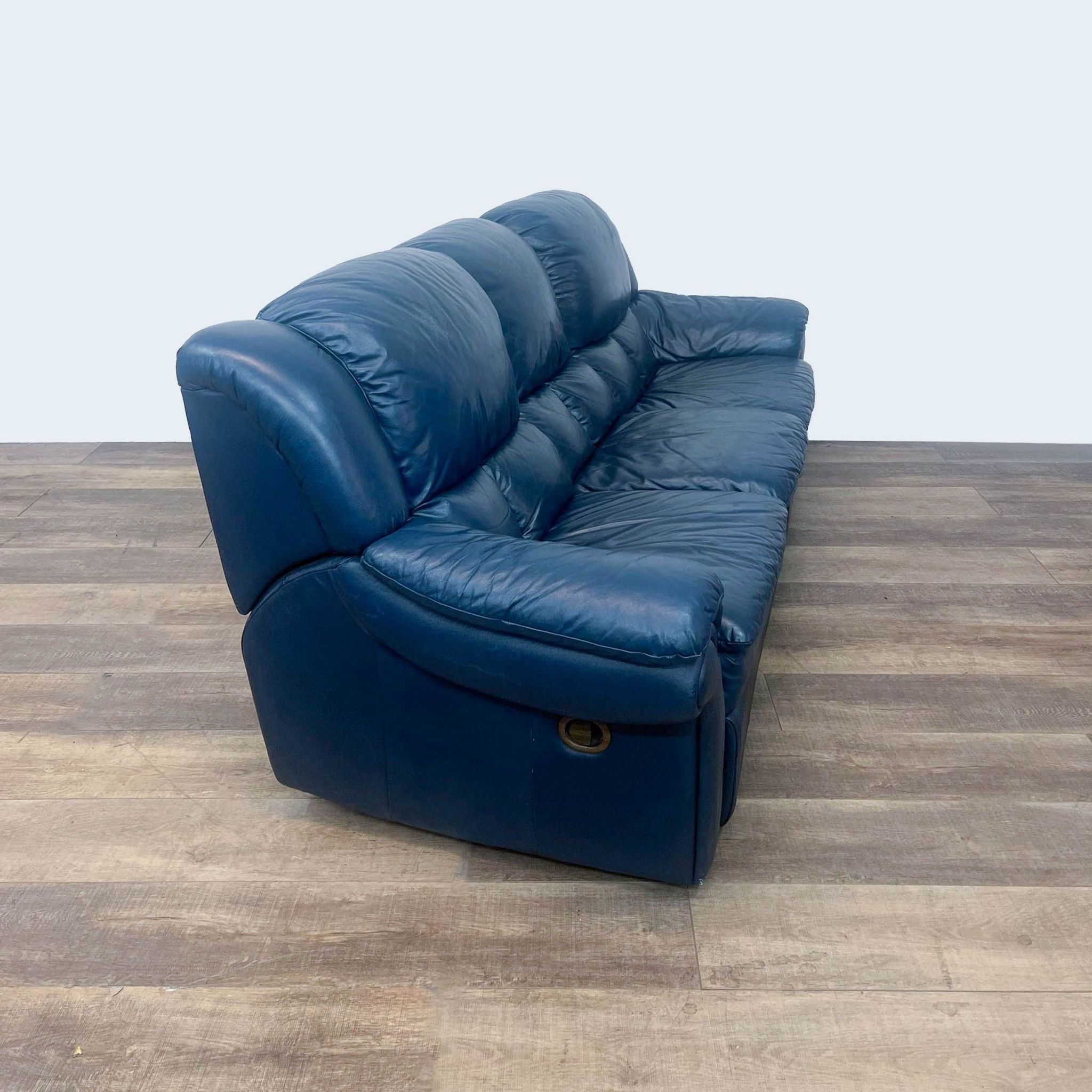 Alt: Dark blue Reperch 94" leather reclining sofa with high back and pillow-top arms on wood floor.