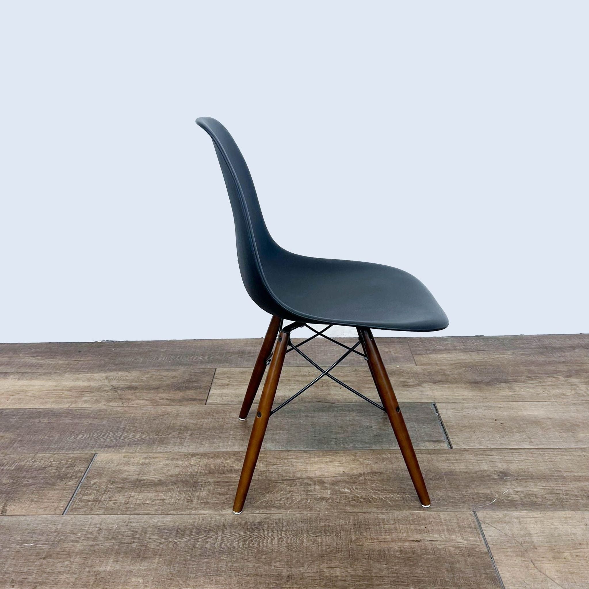 Side angle of a black molded Reperch dining chair with wood and metal base on wooden floor.