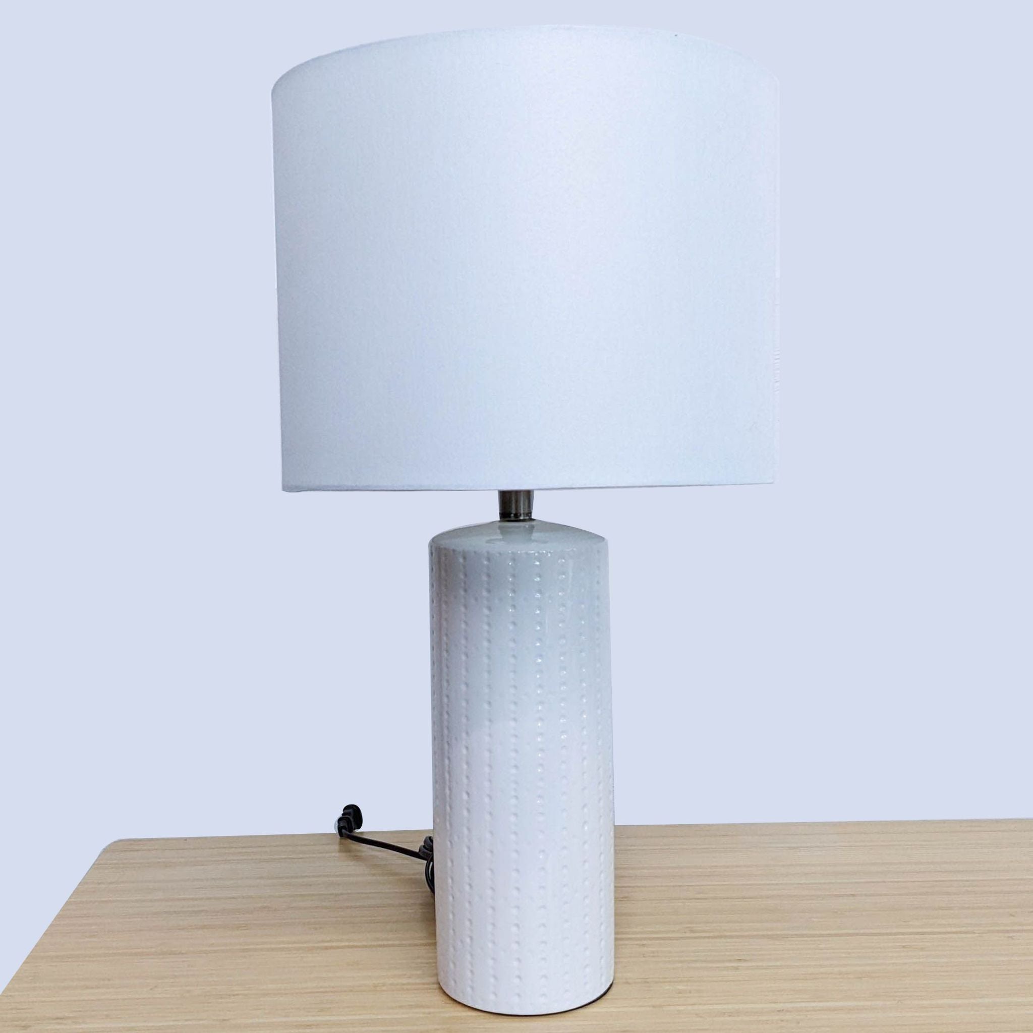 Reperch brand table lamp with a cylindrical base and a white fabric shade on a wooden surface.