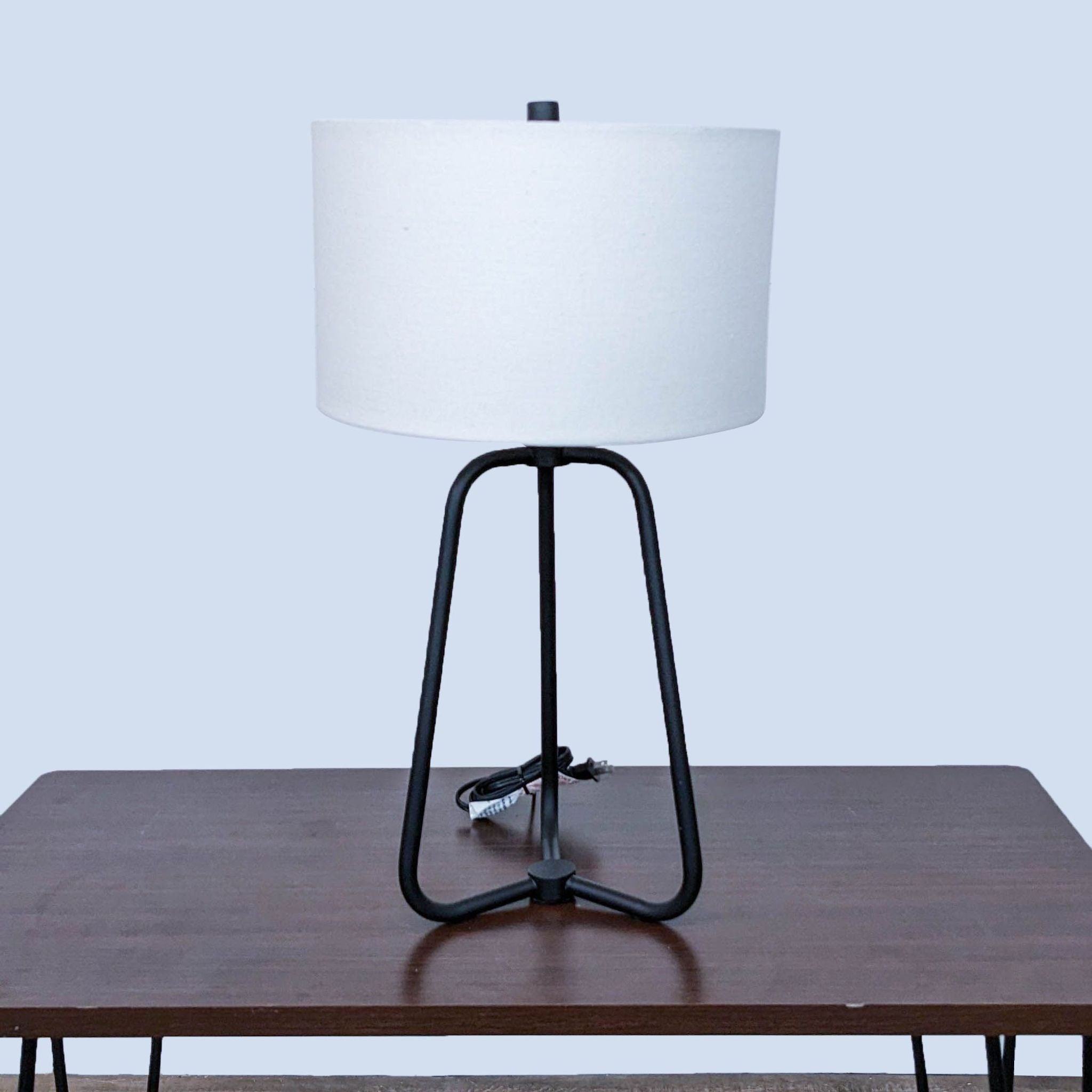 Front-facing view of a Reperch tripod table lamp with cylindrical white shade and black legs.