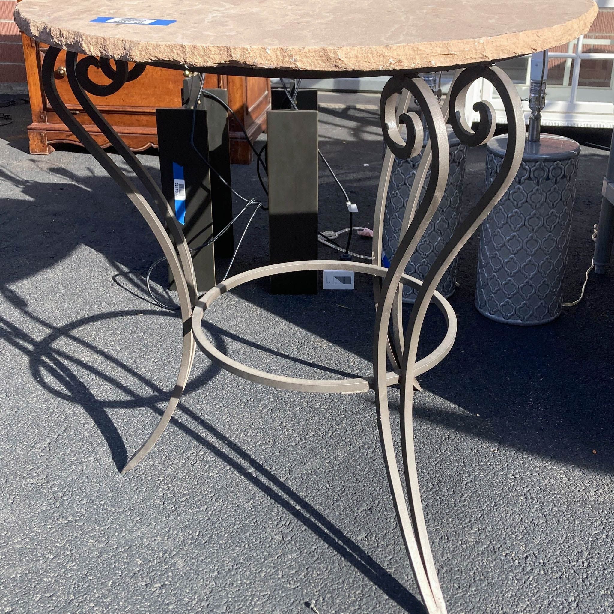 Beige textured round table by Reperch with intricate metal leg design and shadow on ground.