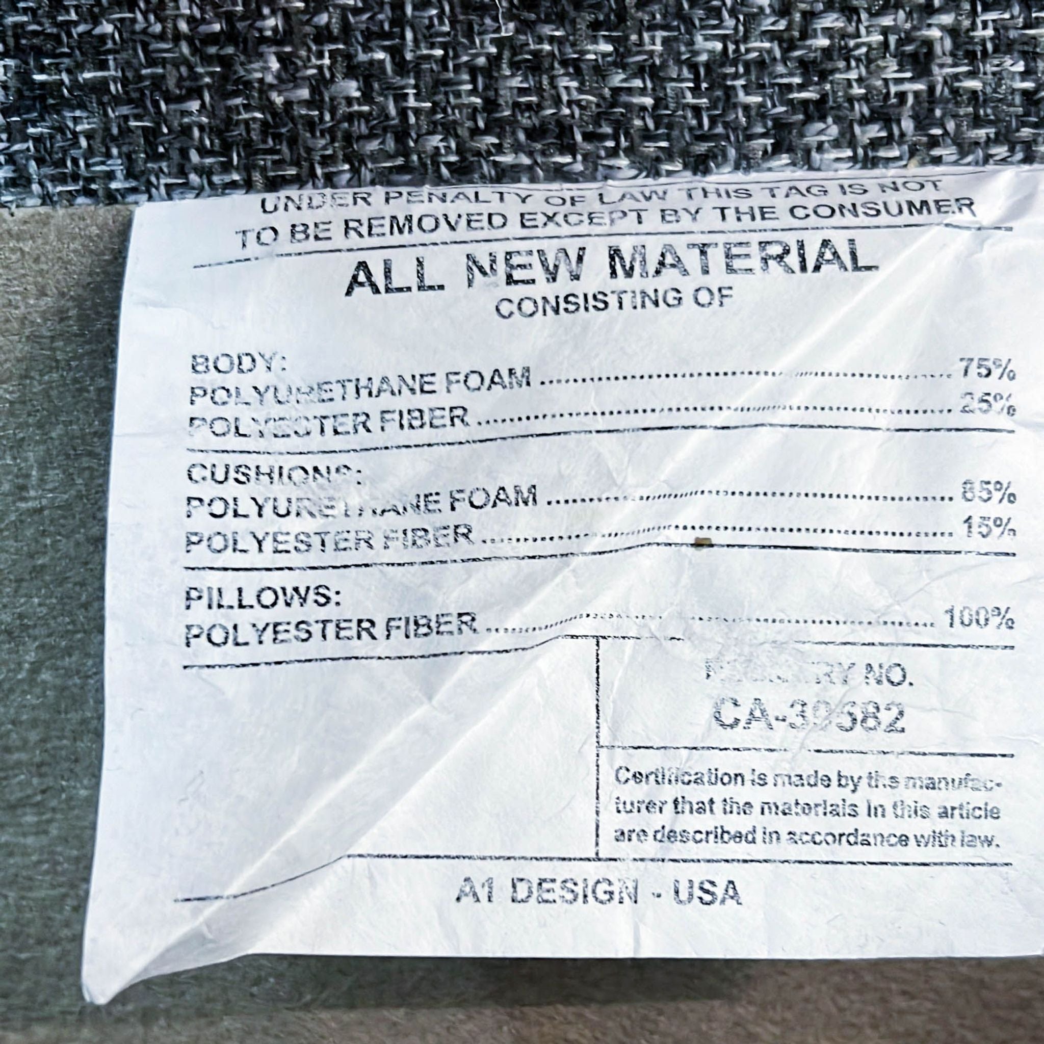 Alt text: Close-up of a material content tag showing polyurethane foam and polyester fiber composition, on a textured gray sectional sofa.
