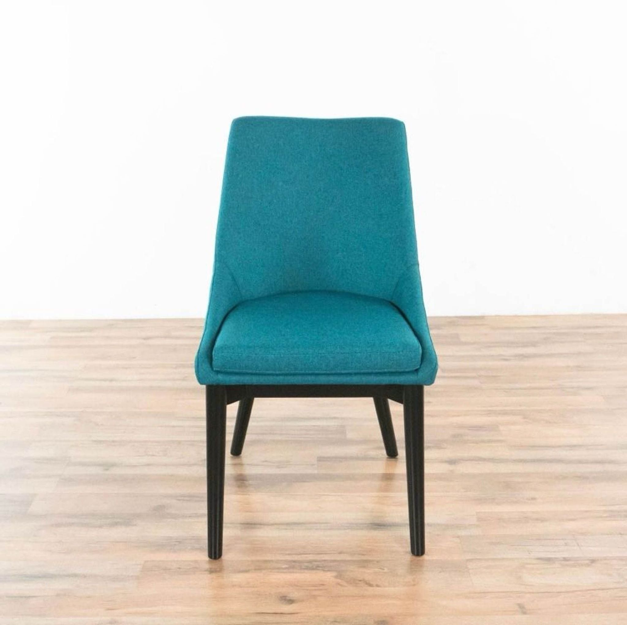 Front view of a teal StealMod Viscount side chair with dense foam padding and tapered black wood legs on a wooden floor.