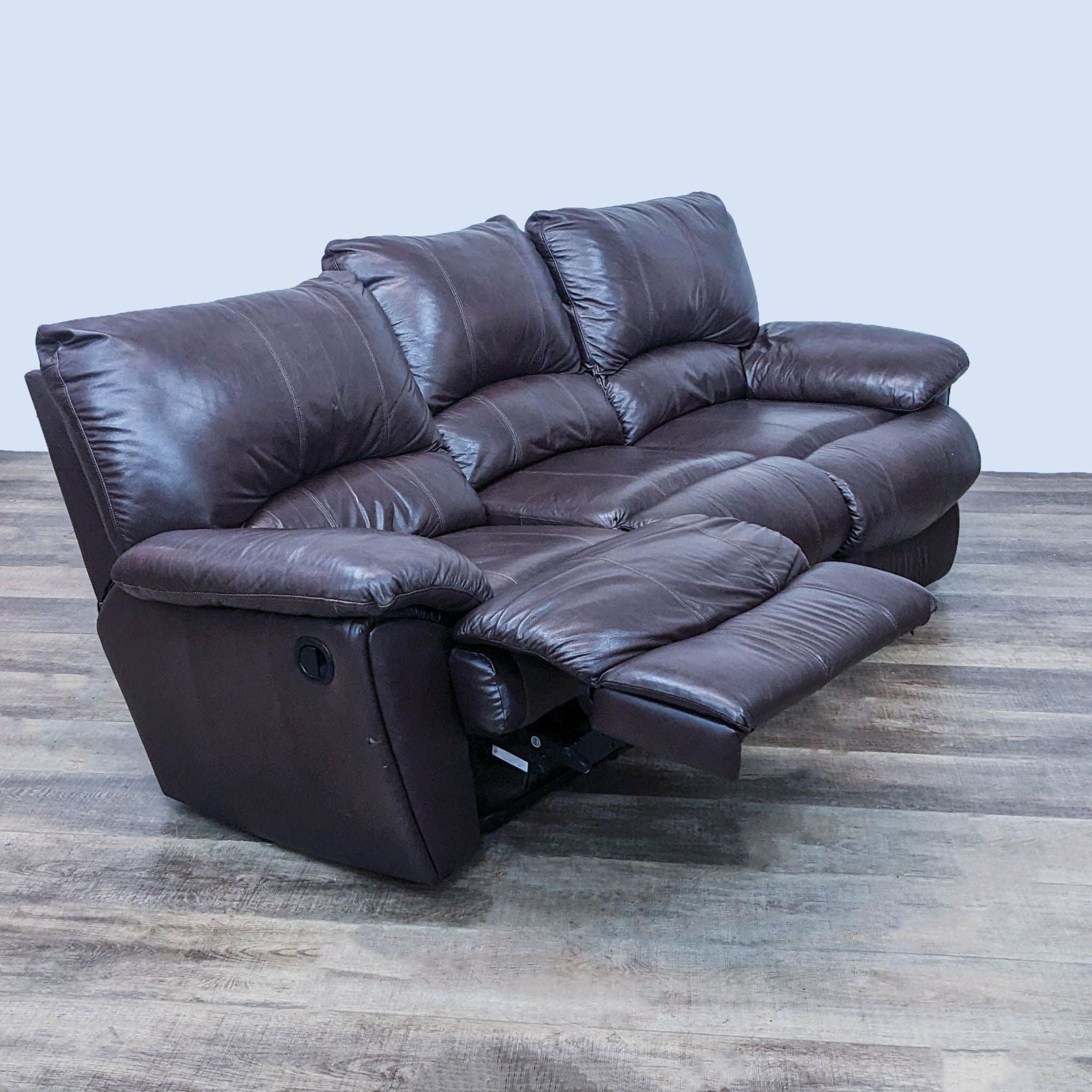 Reclined high back, dark brown, leather-look 3-seat sofa by Reperch with plush pillow-top arms on a wood-patterned floor.