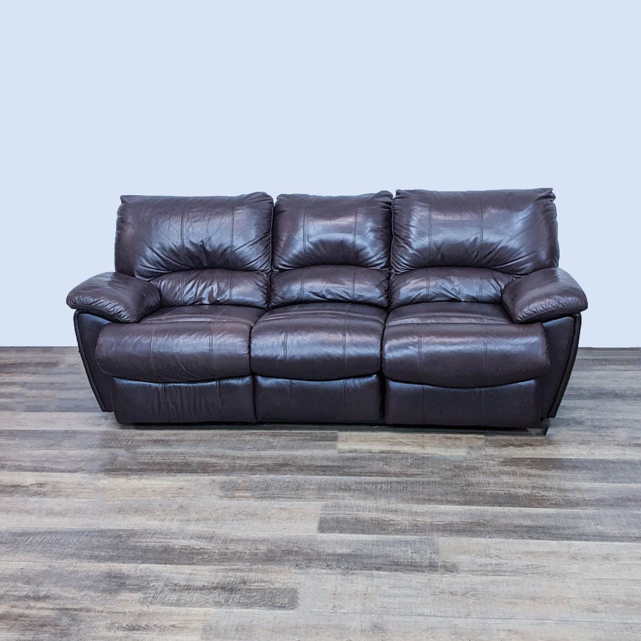 Three-seater Reperch sofa featuring high back and cushioned pillow-top arms in a leather look, fully reclined on one end, against a wood-style floor.