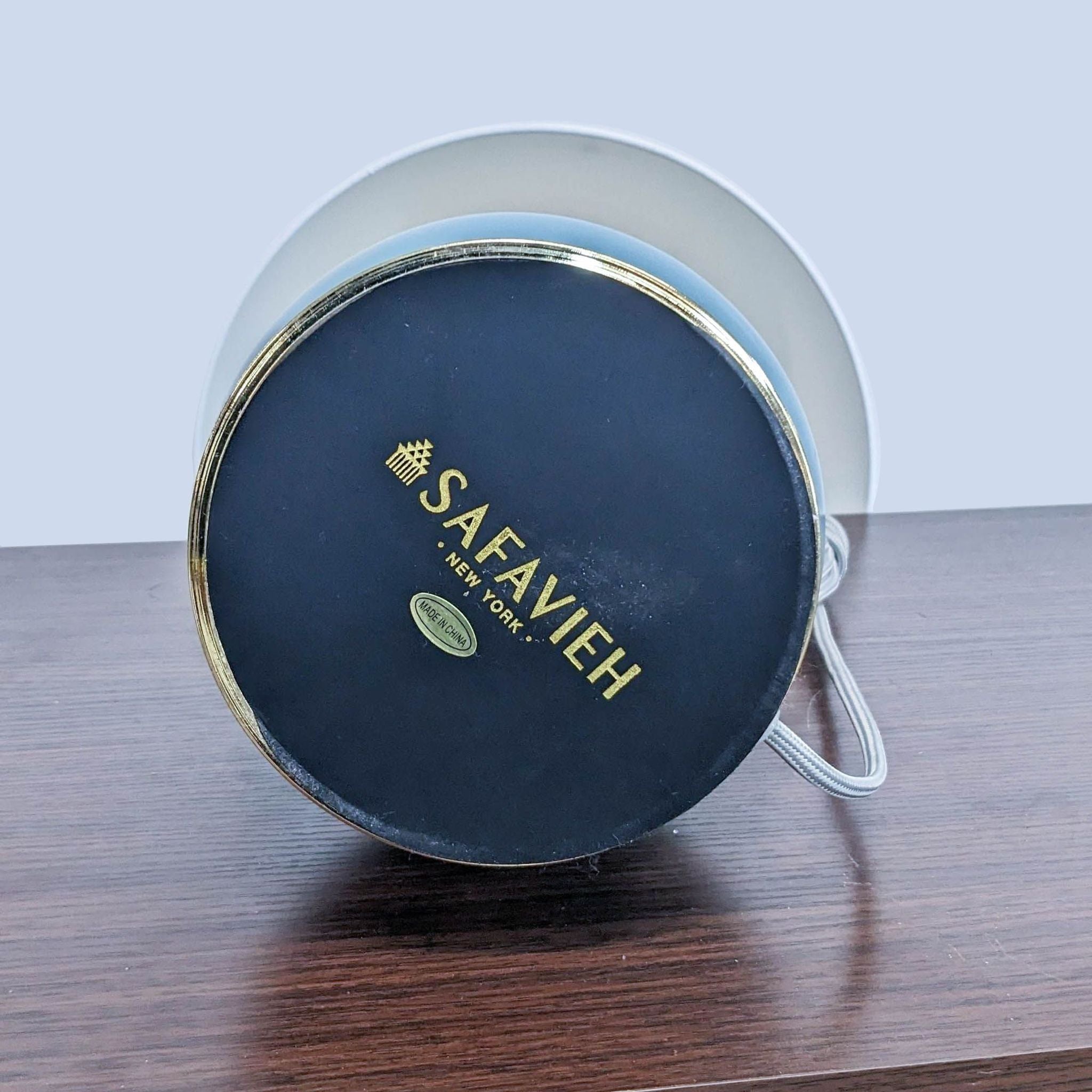 Alt text 2: "Bottom view of a Safavieh lamp showcasing the brand's logo on the black surface with a gold rim and power cable."