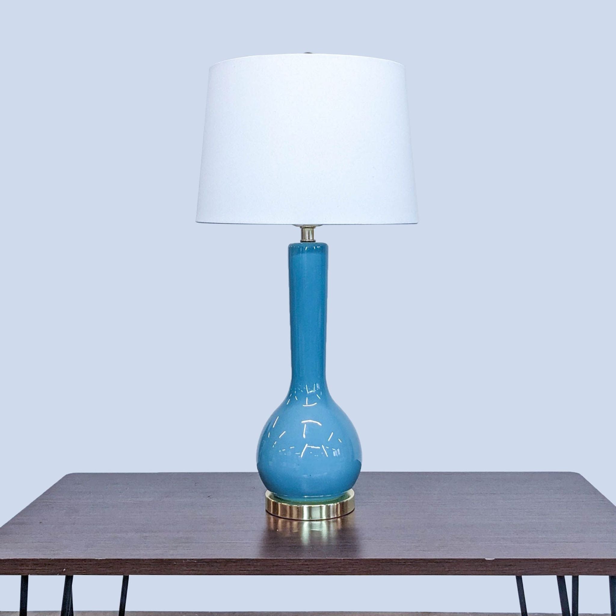 Safavieh lighting category, blue ceramic table lamp with white shade on wooden table, neutral background.