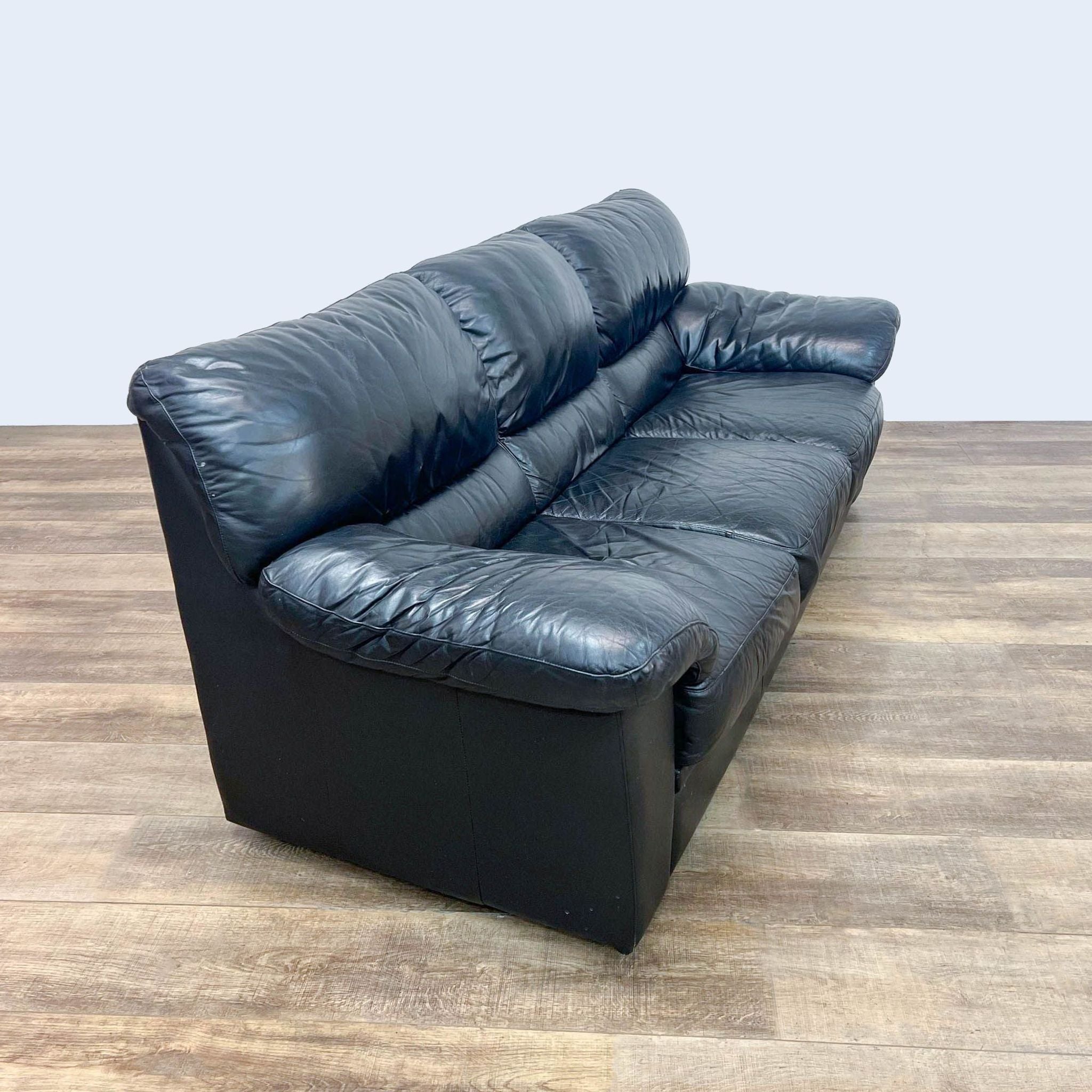 Reperch brand contemporary black leather three-seat sofa with pillow top arms on a wooden floor.