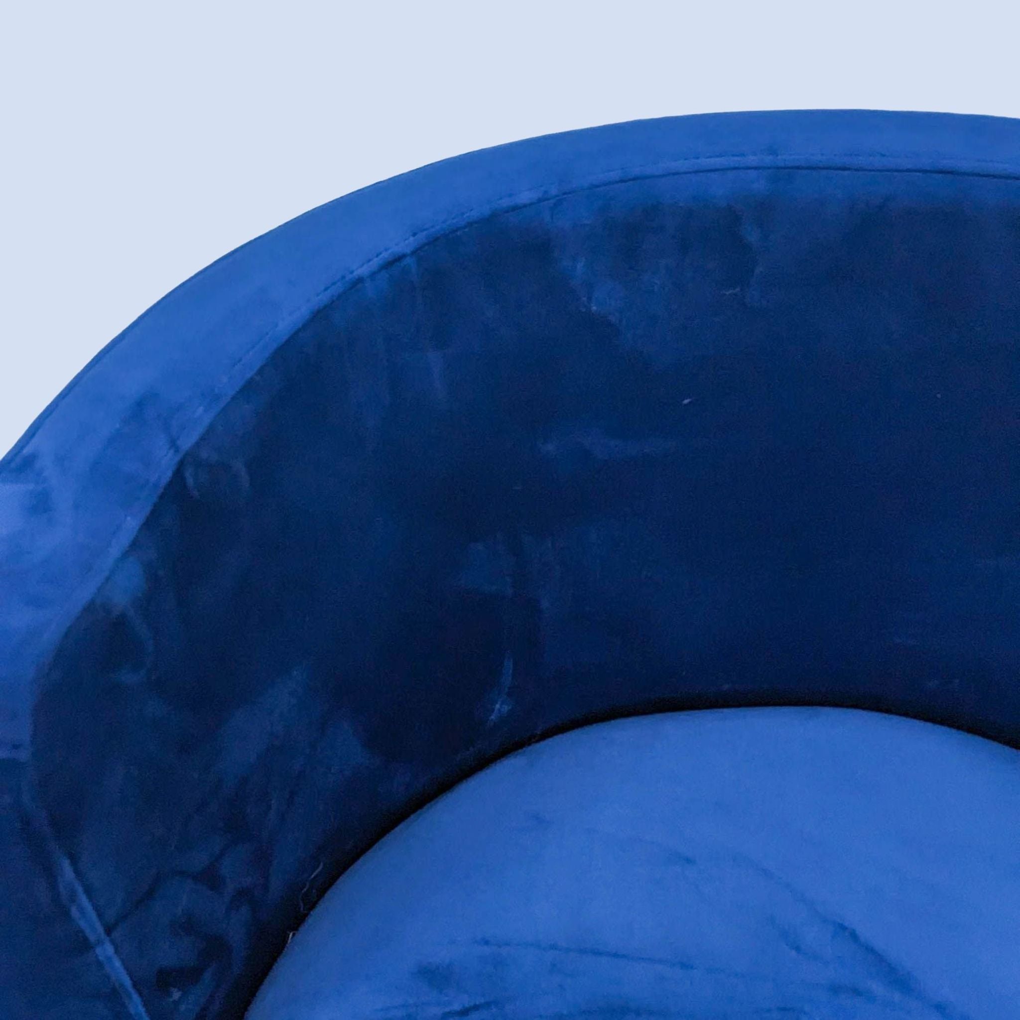 Close-up view of a navy blue velvet dining chair's rounded backrest, highlighting the rich texture and color.