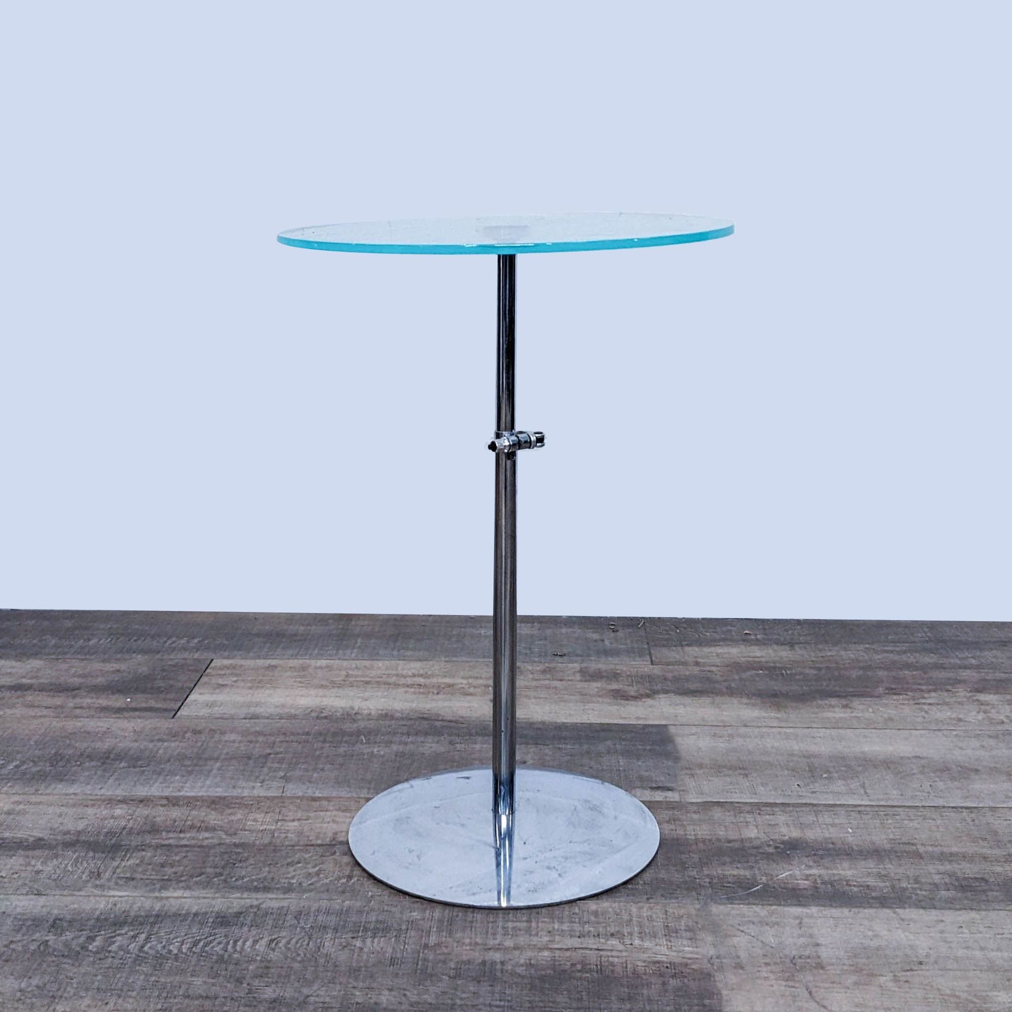Crate & Barrel side table with a round glass top on a chrome pedestal base, against a wooden floor background.