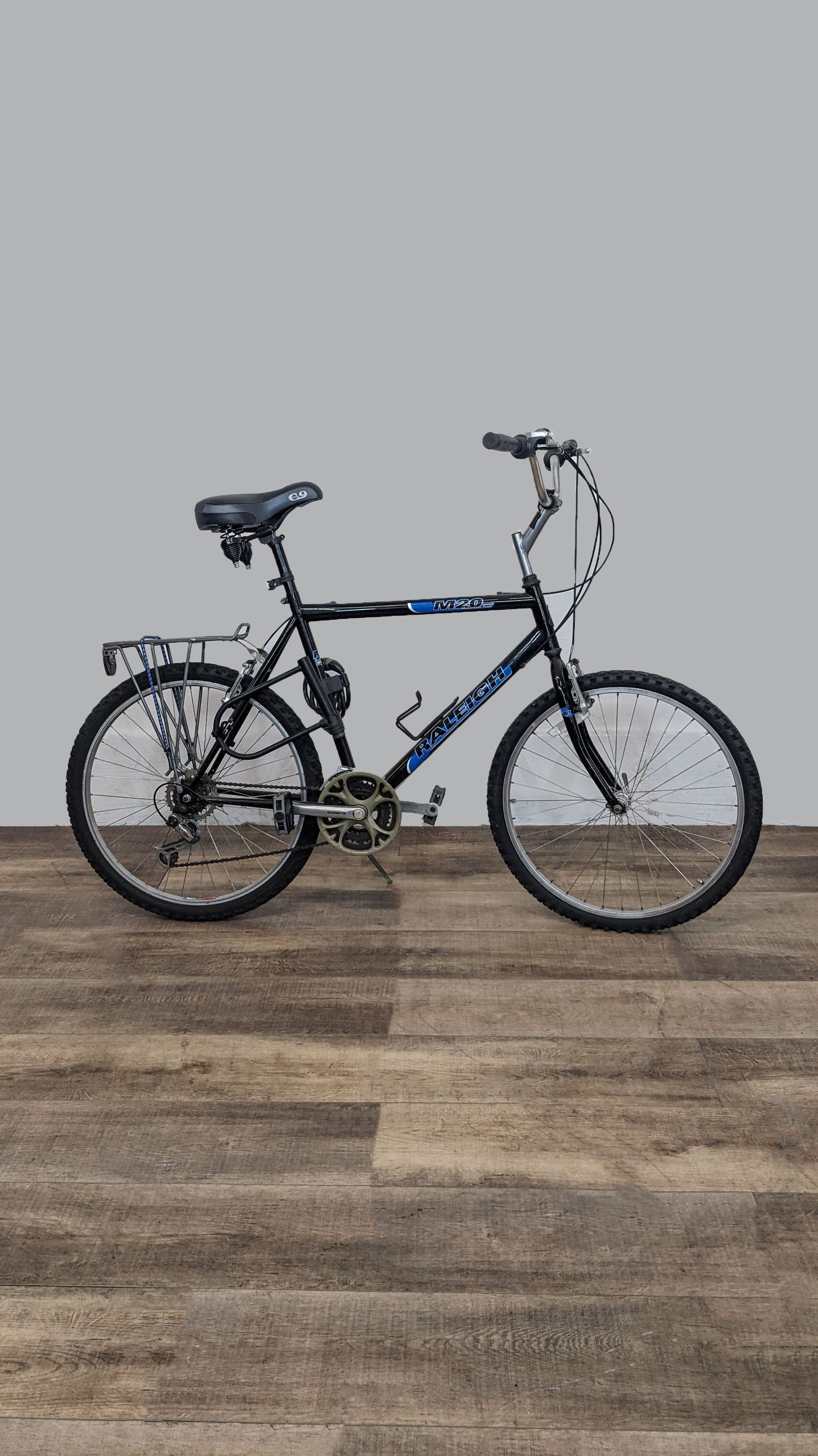 Raleigh mountain bike with black frame and blue decals on wooden floor.