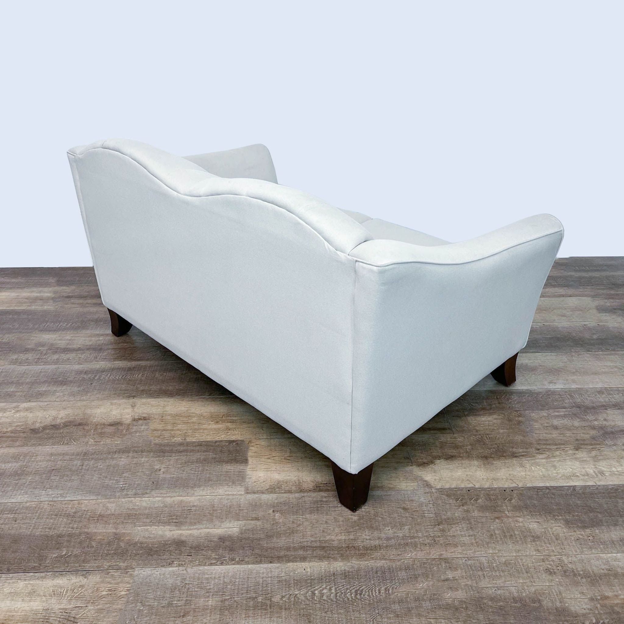 Bauhaus Furniture loveseat with tufted back, sloped arms, and dark finish feet on a wooden floor.