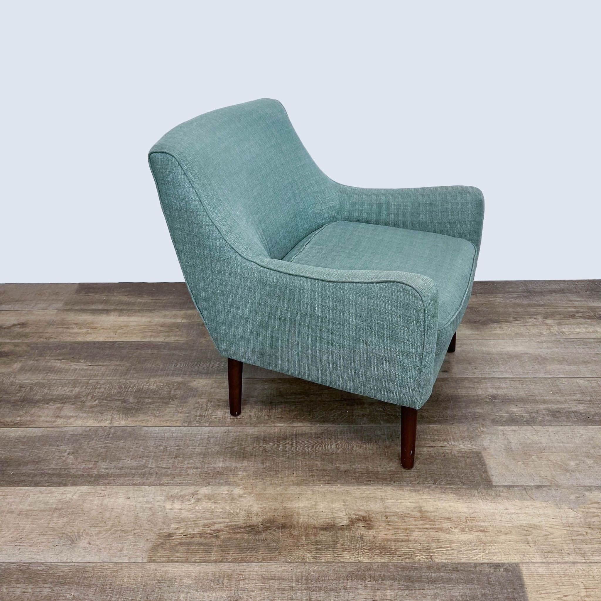 A side perspective of the Madison Park Liam chair, highlighting its mid-century design with angled wooden legs and green fabric.