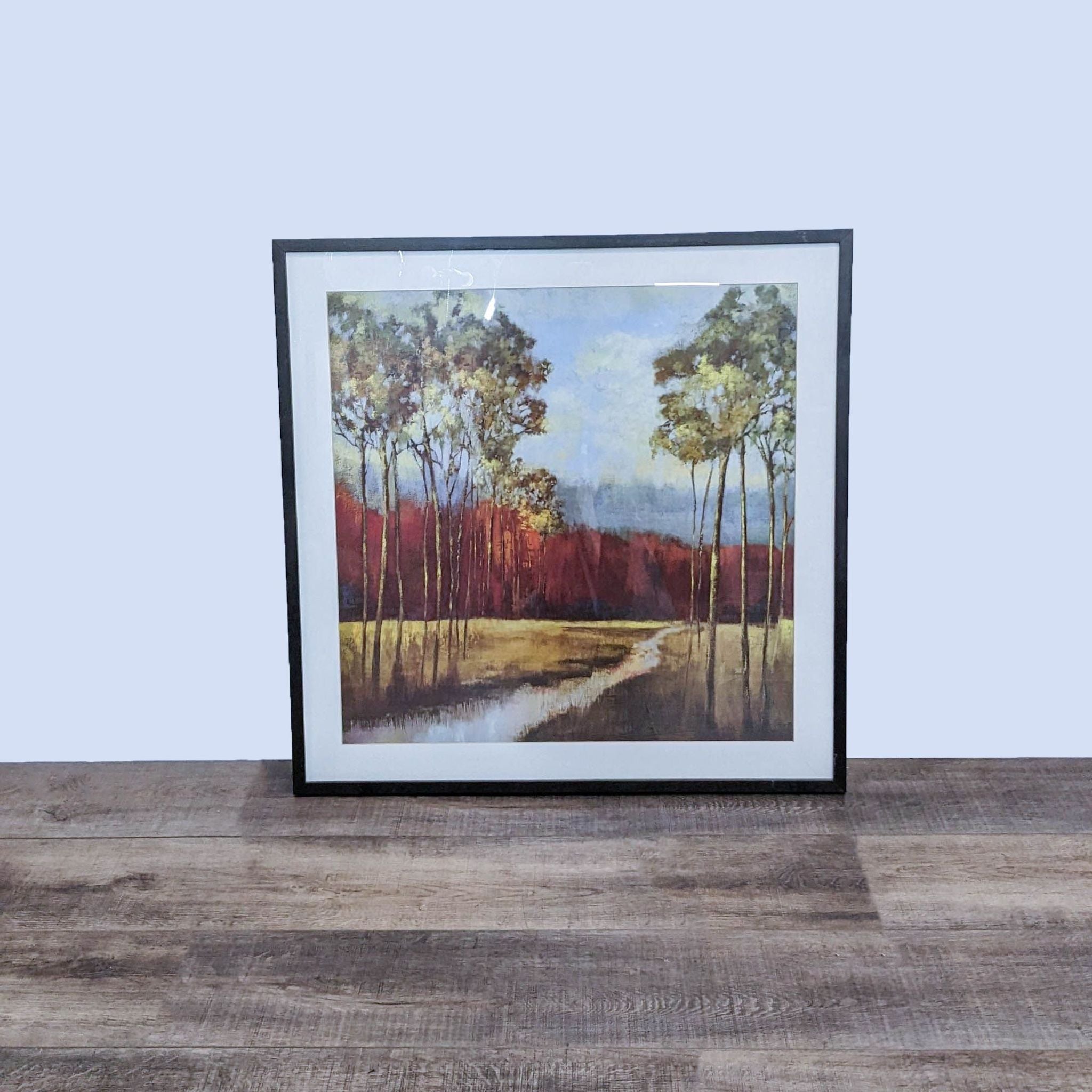 Framed landscape painting by Art.com with trees and reflective water on a wooden floor.