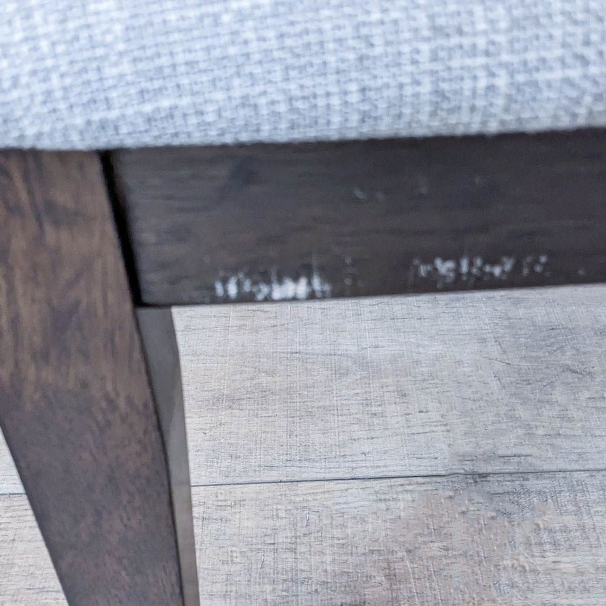 Close-up of a Reperch contemporary dining chair leg with dark finish and part of the grey upholstered seat visible.