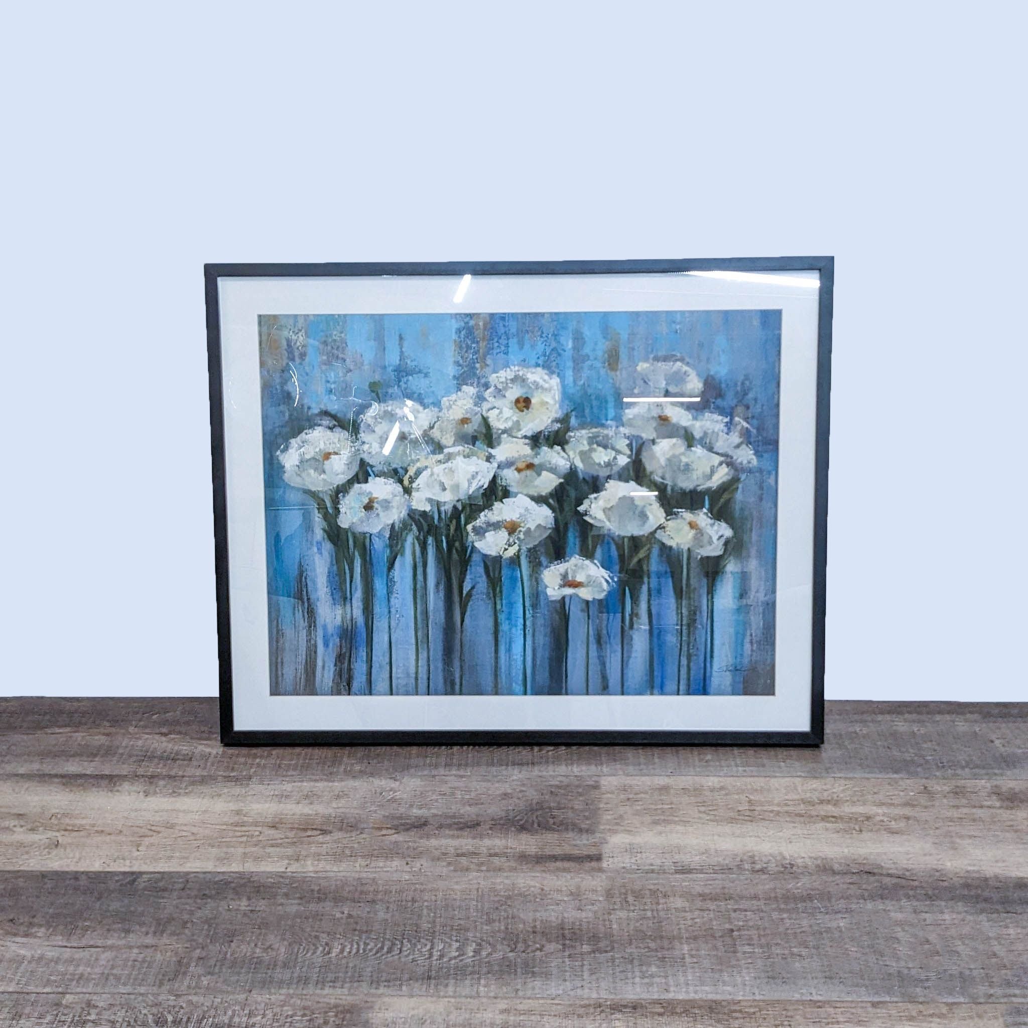 Framed floral painting by Art.com craftsman on table, featuring white flowers against a blue background.
