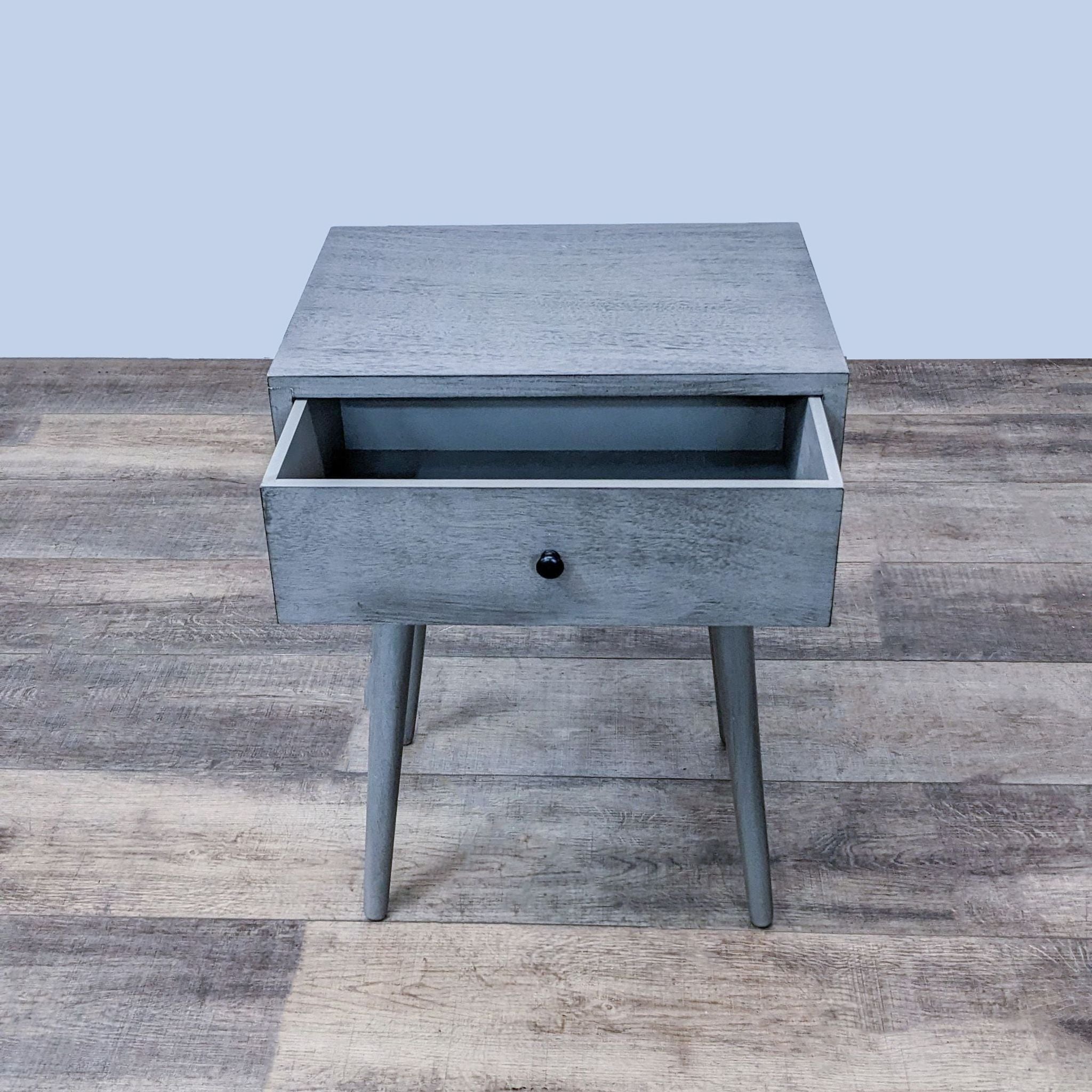 Gray Reperch end table with the drawer open, revealing storage space, on a textured wooden floor.