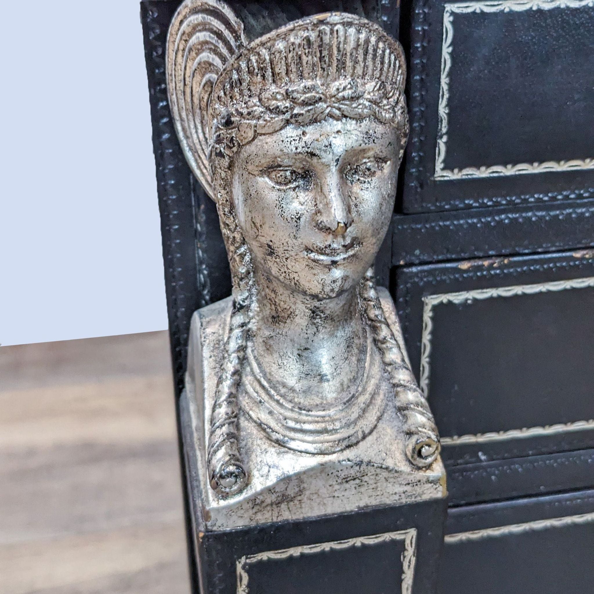 Close-up of an Egyptian Revival style corner detail on a Maitland Smith multi-drawer leather chest with a carved face and gold trim.