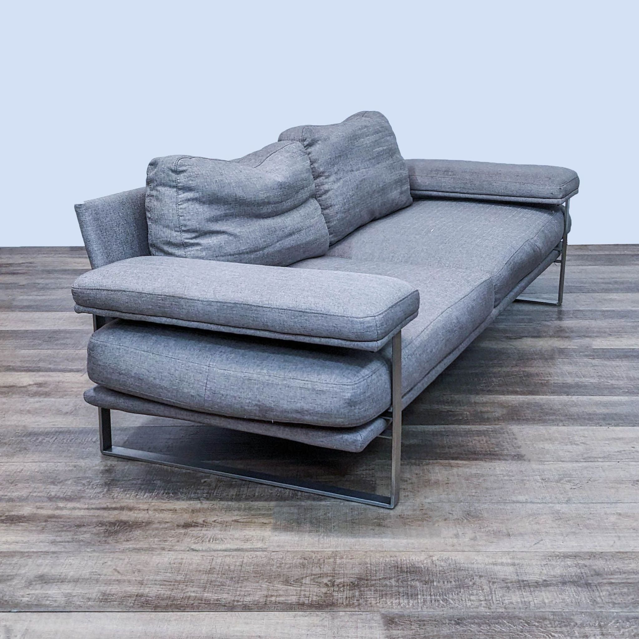 Side perspective of a gray fabric 3-seat Reperch sofa with metal framing and extended chaise, on wood flooring.