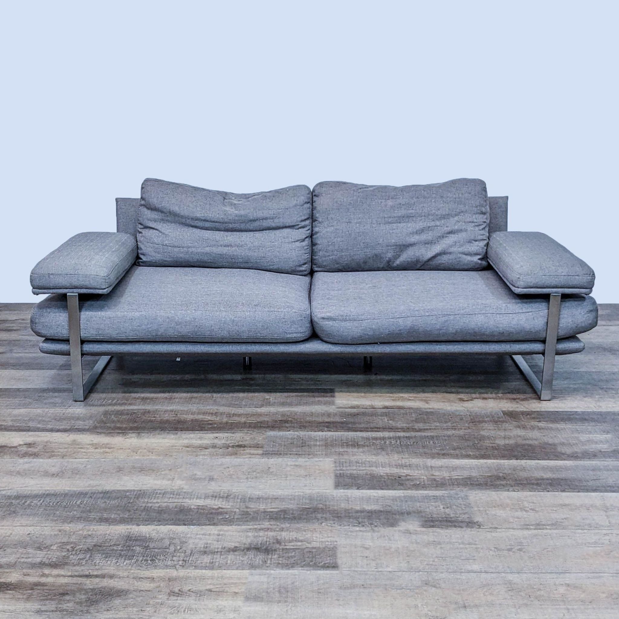 Reperch brand 3-seat upholstered sofa in gray with brushed chrome frame, frontal view on wooden floor.
