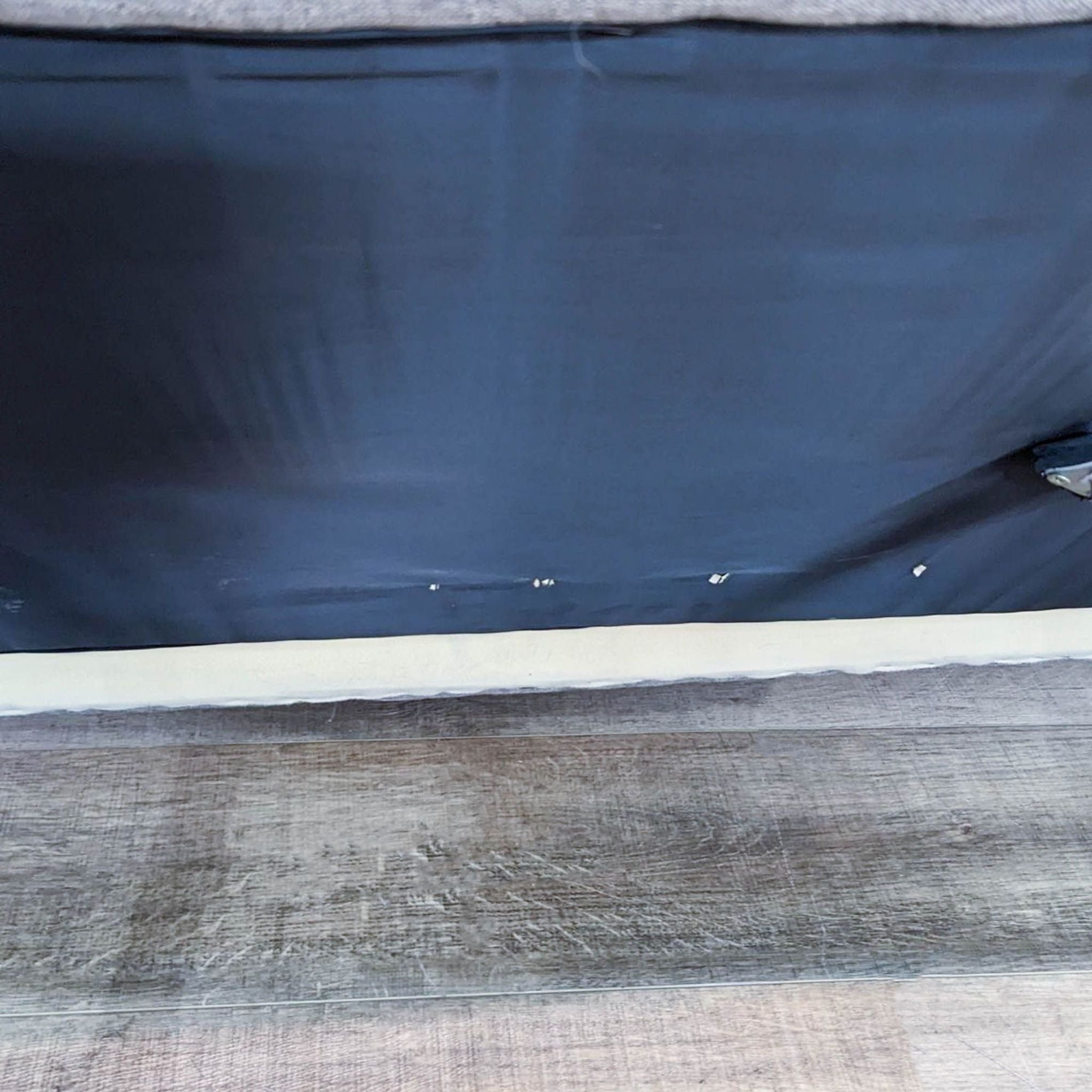 Close-up of the underside of a gray Reperch upholstered sofa showing the fabric cover and floor.