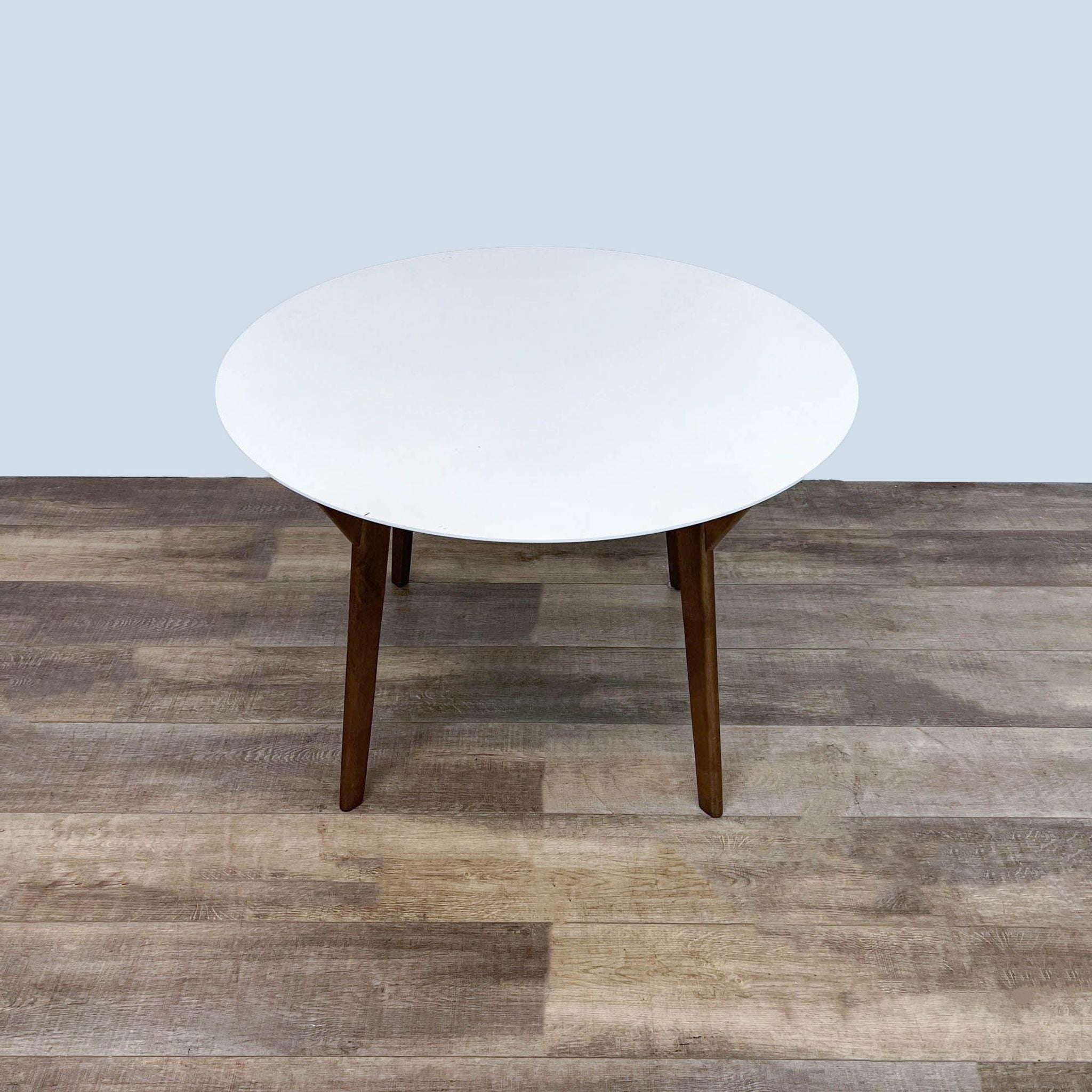 Modern Wegmans round white dining table with solid wood legs against neutral background for a clean look.