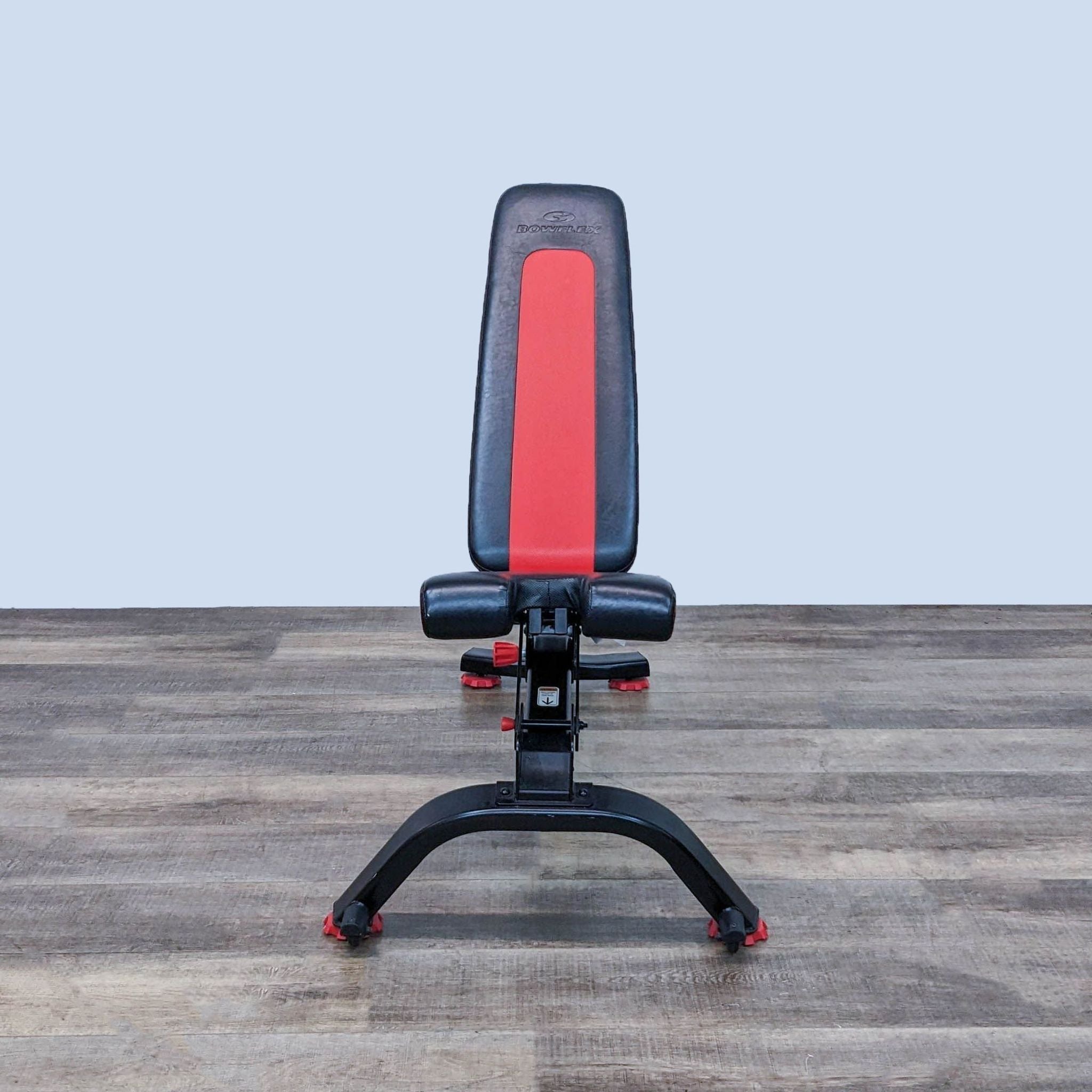 Alt text 1: Bowflex workout bench in an upright position on a wooden floor, showcasing the brand logo and red and black design.