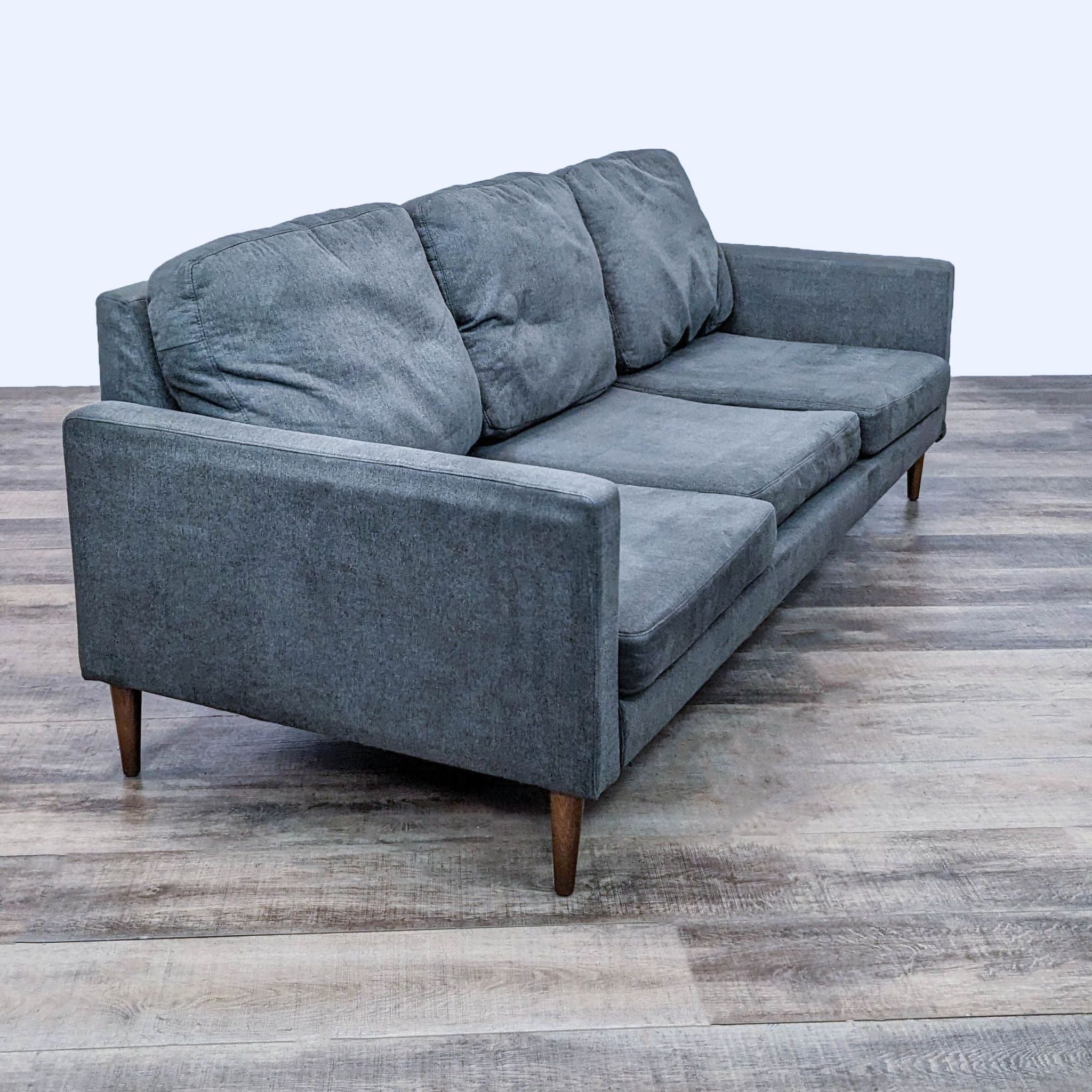 2. Side angle view of a modern Reperch 3-seat gray sofa showing its sleek lines and tapered wooden feet on a wooden floor.