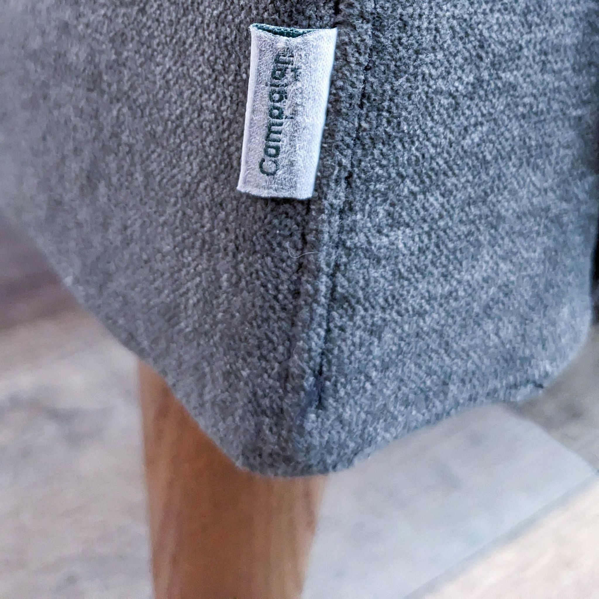 3. Close-up of a gray upholstered Reperch sofa's leg, featuring a clean design with a visible brand label on the side.