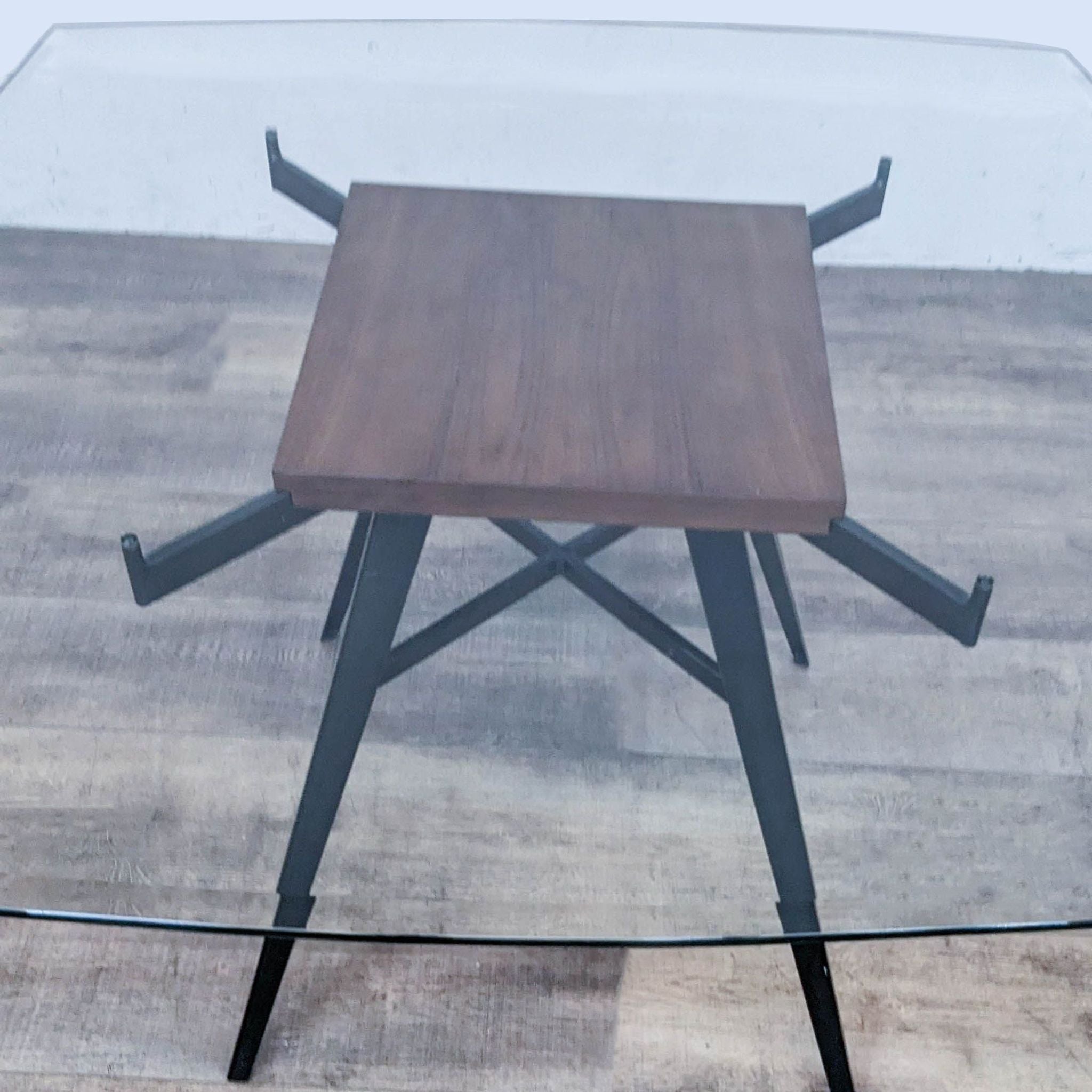 Contemporary Armen Living Ojai dining table with a clear glass top showcasing a mineral-finish metal base, set against a wood-style backdrop.