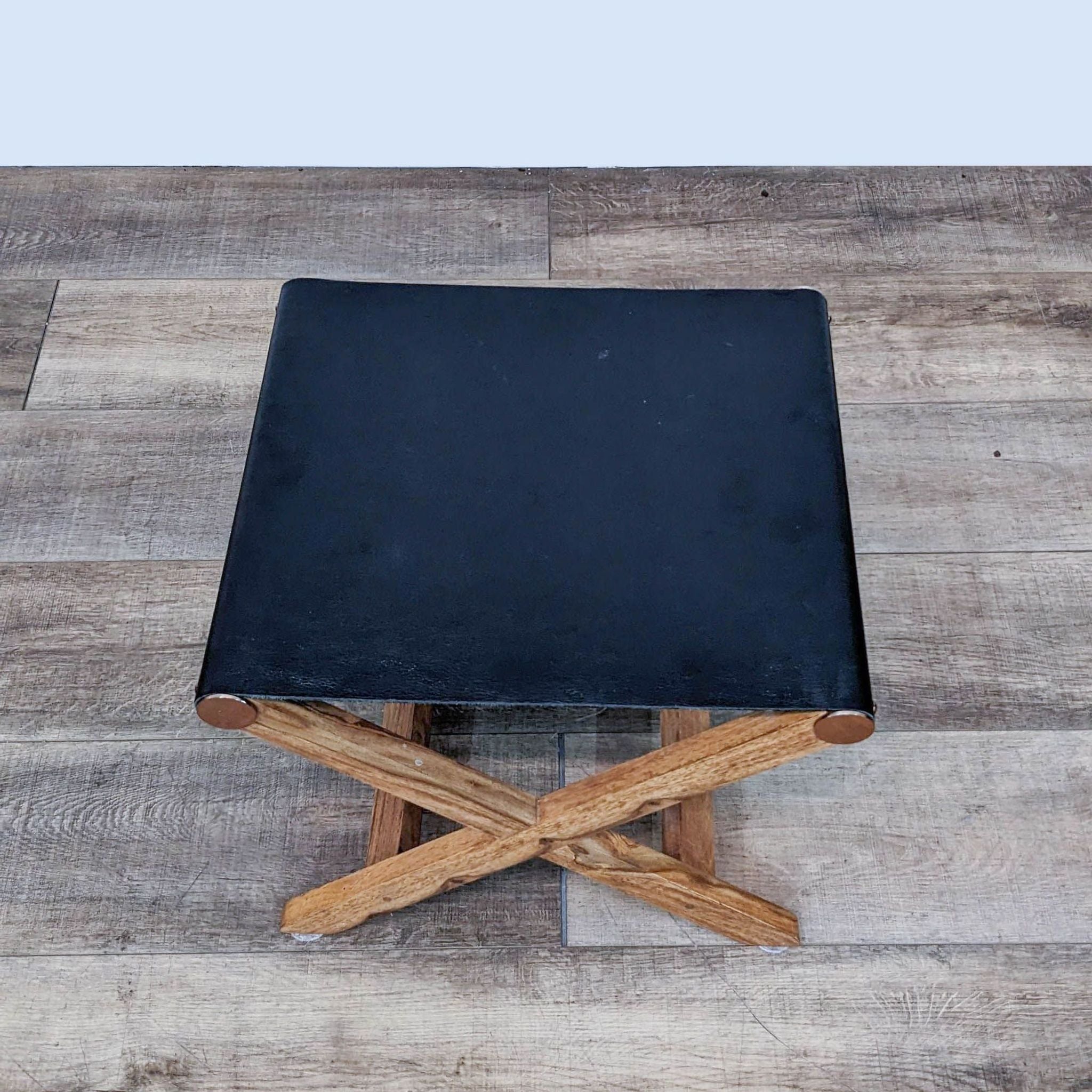 CB2 modern ottoman with black leather seat on crisscrossed solid wood frame and metal accents.