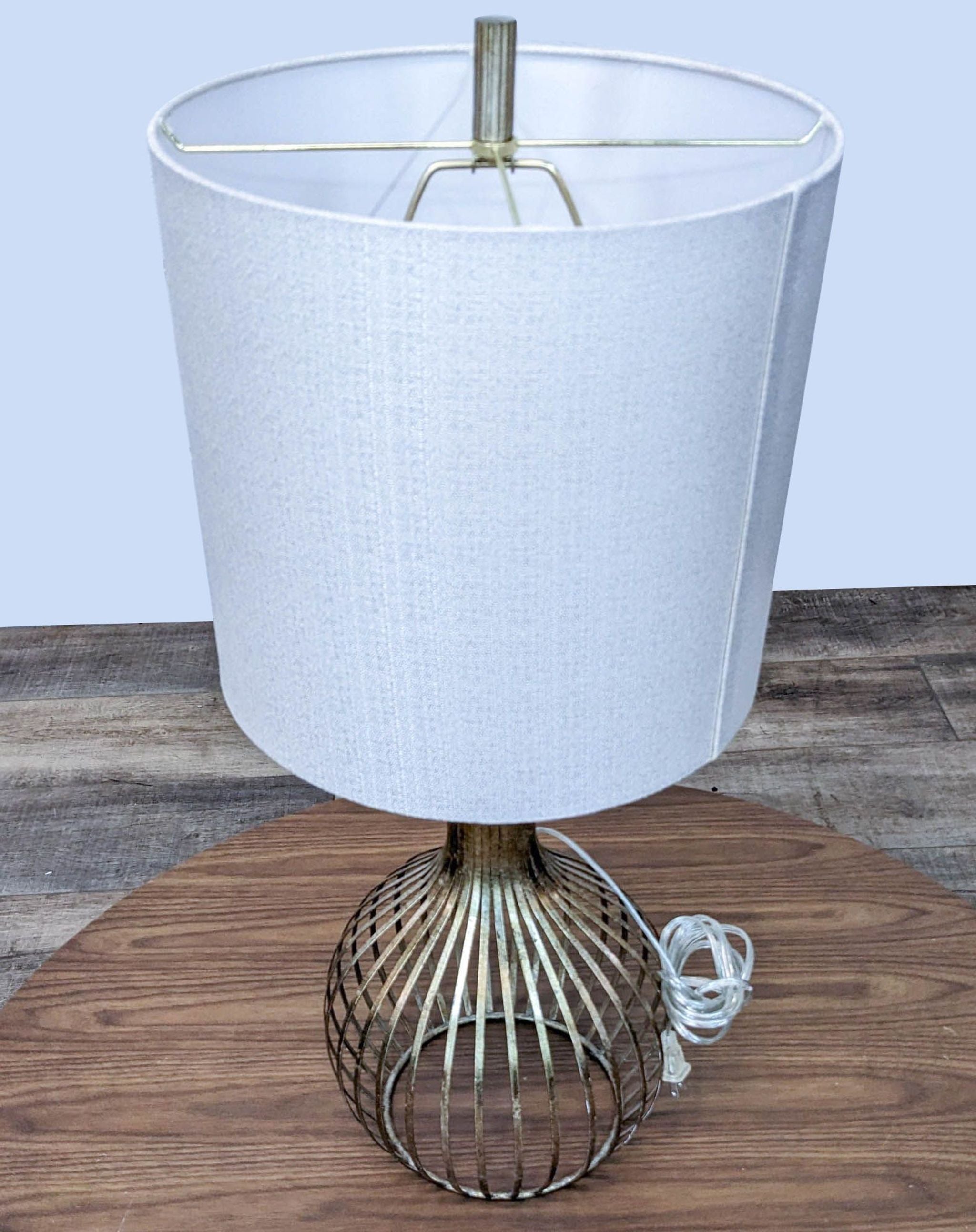 Reperch lighting table lamp with a white fabric shade and a bronze-finished cage base, unplugged on wood floor.