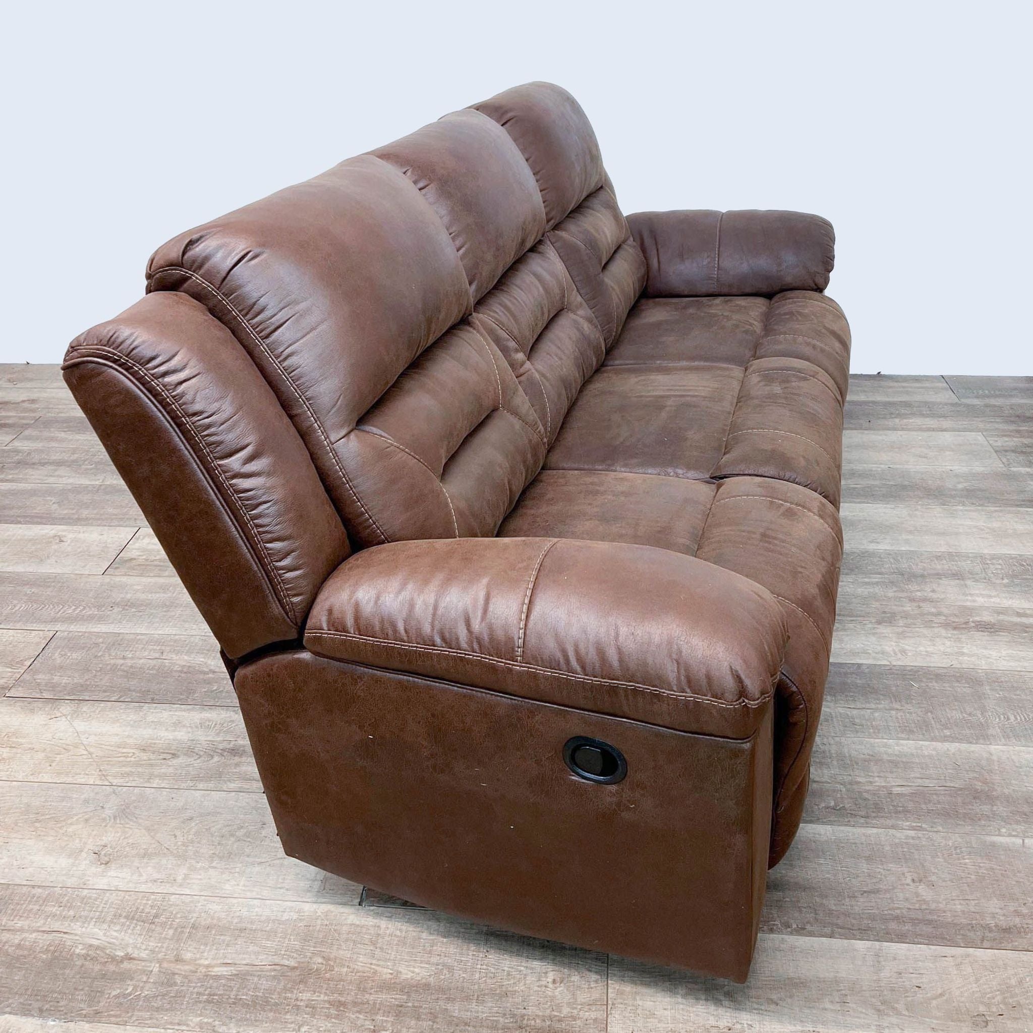 Saddle brown, leather-look, high-back Reperch 3-seat dual reclining sofa with pillow top arms on a wooden floor.
