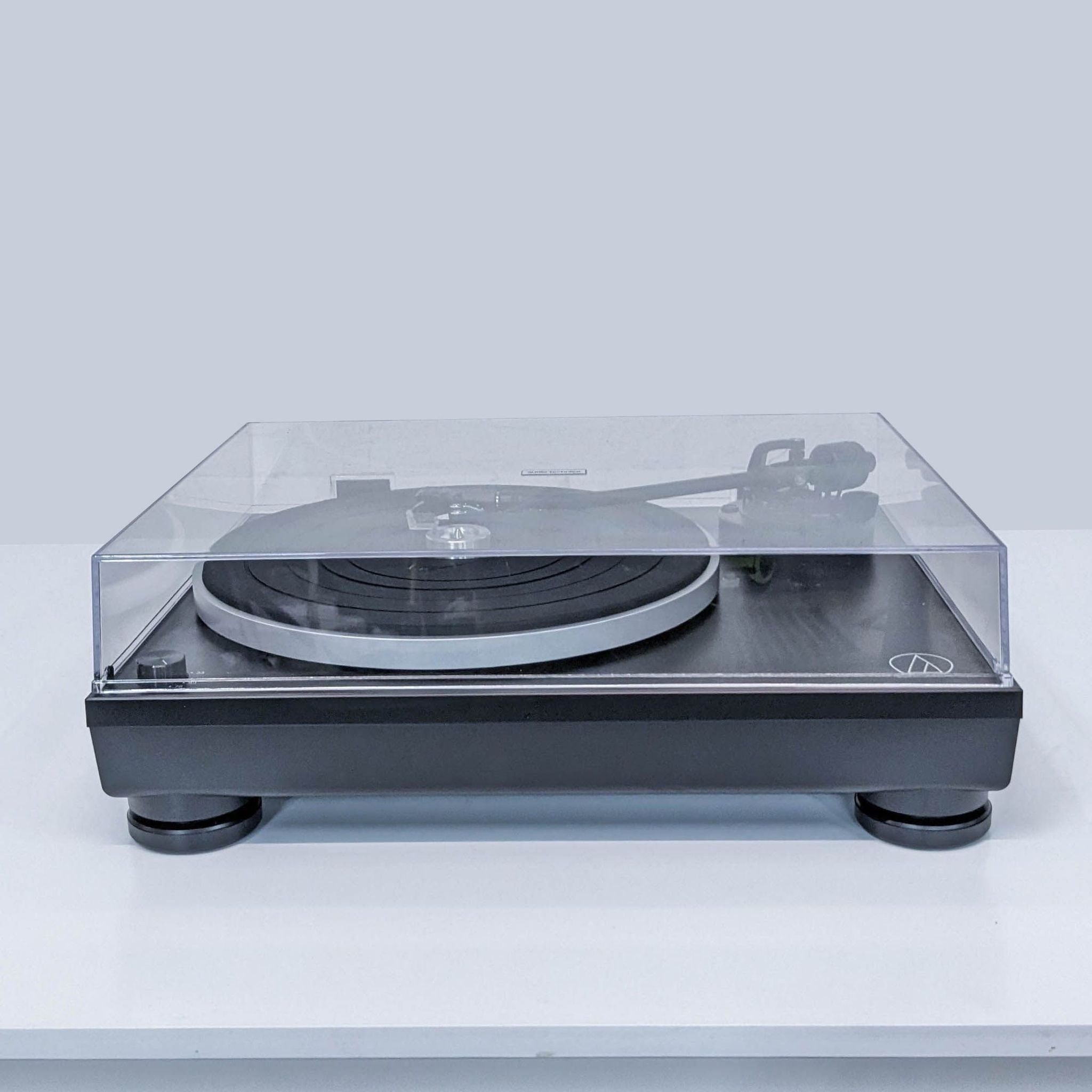 Audio-Technica turntable with transparent dust cover on a gray surface.