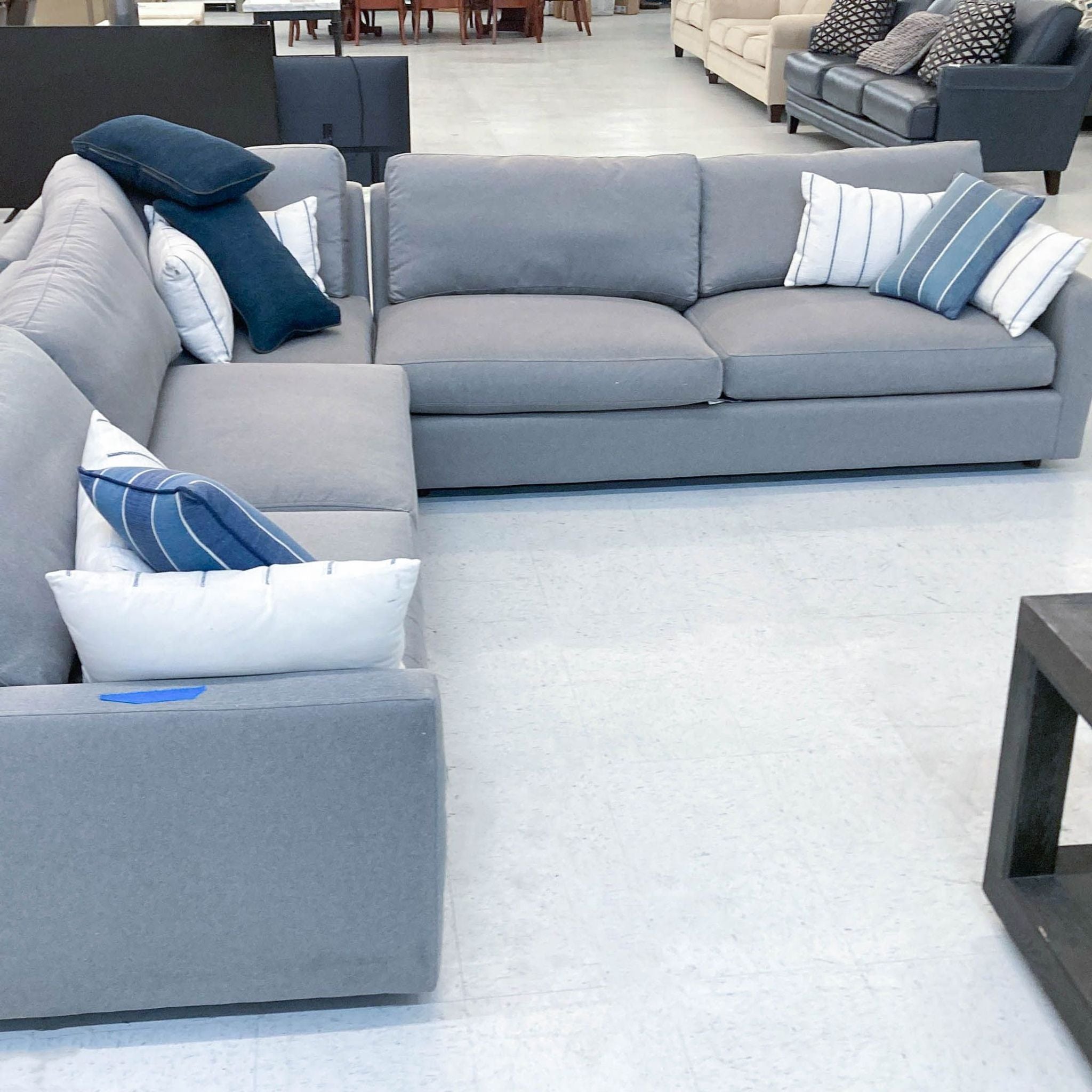 2. L-shaped gray sectional by Room & Board with white and blue accent pillows, displayed in a showroom.