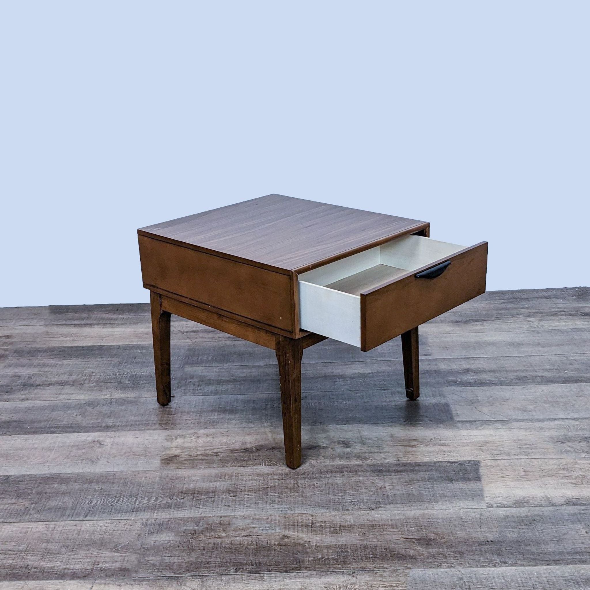 Reperch wooden end table with an open drawer revealing a white interior, set on a wood grain floor with a plain backdrop.