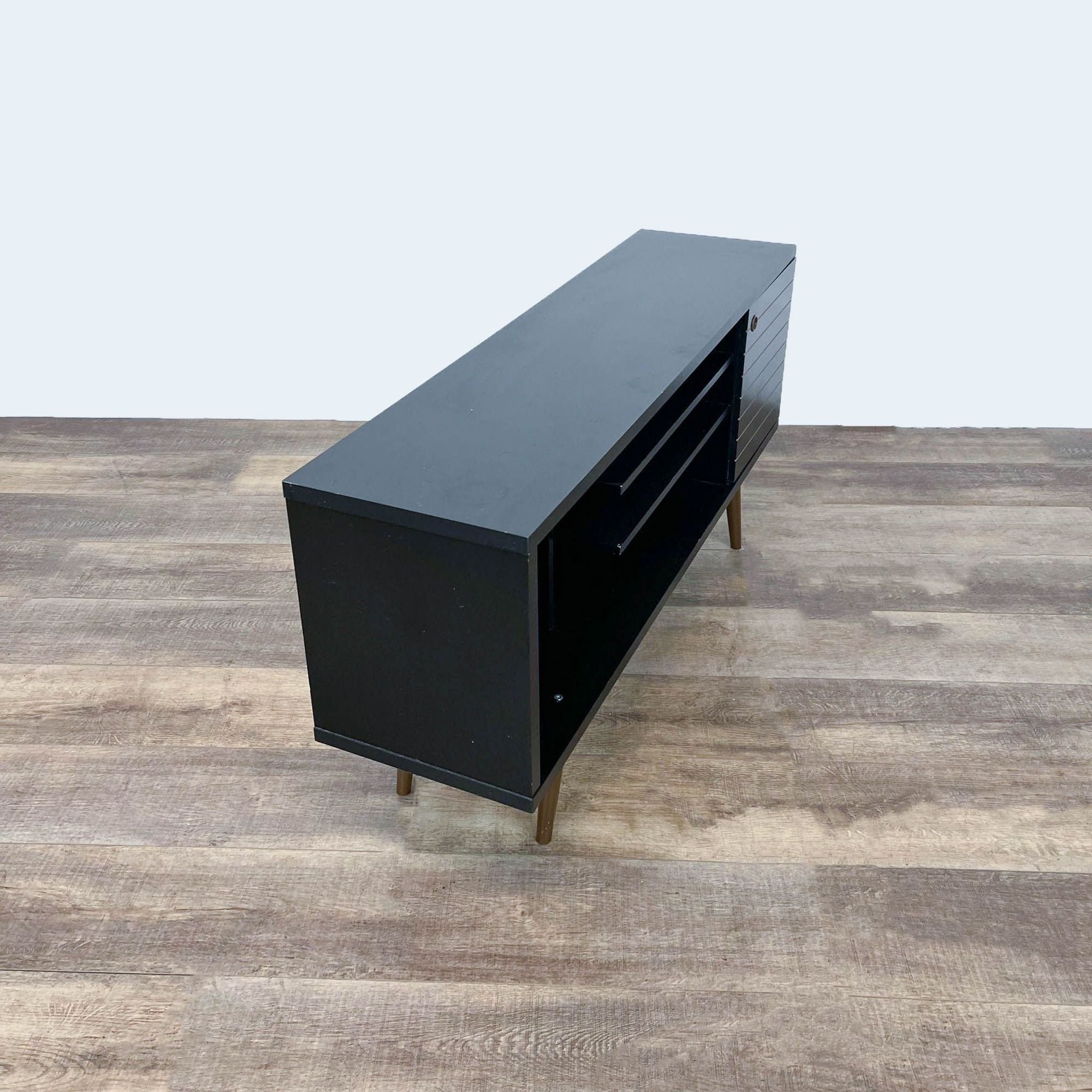 Black Reperch entertainment center with open drawers on a wooden floor.